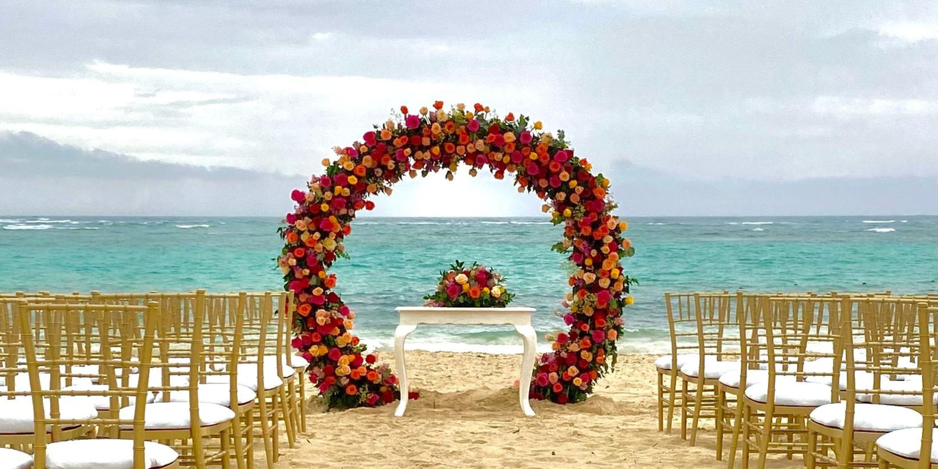 A floral arch and rows of chairs await a destination wedding on the beach at Hotel Riu Palace Bavaro.