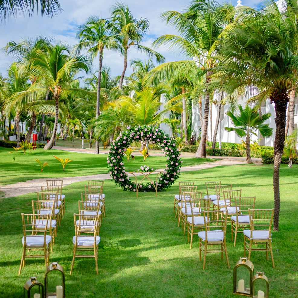 Rows of chairs are arranged on grass facing a floral arch, prepared for a destination wedding ceremony.