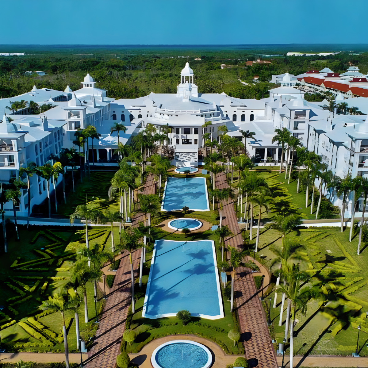 Aerial view of Hotel Riu Palace Punta Cana, perfect for destination weddings, with symmetrically arranged swimming pools surrounded by lush gardens and white buildings.