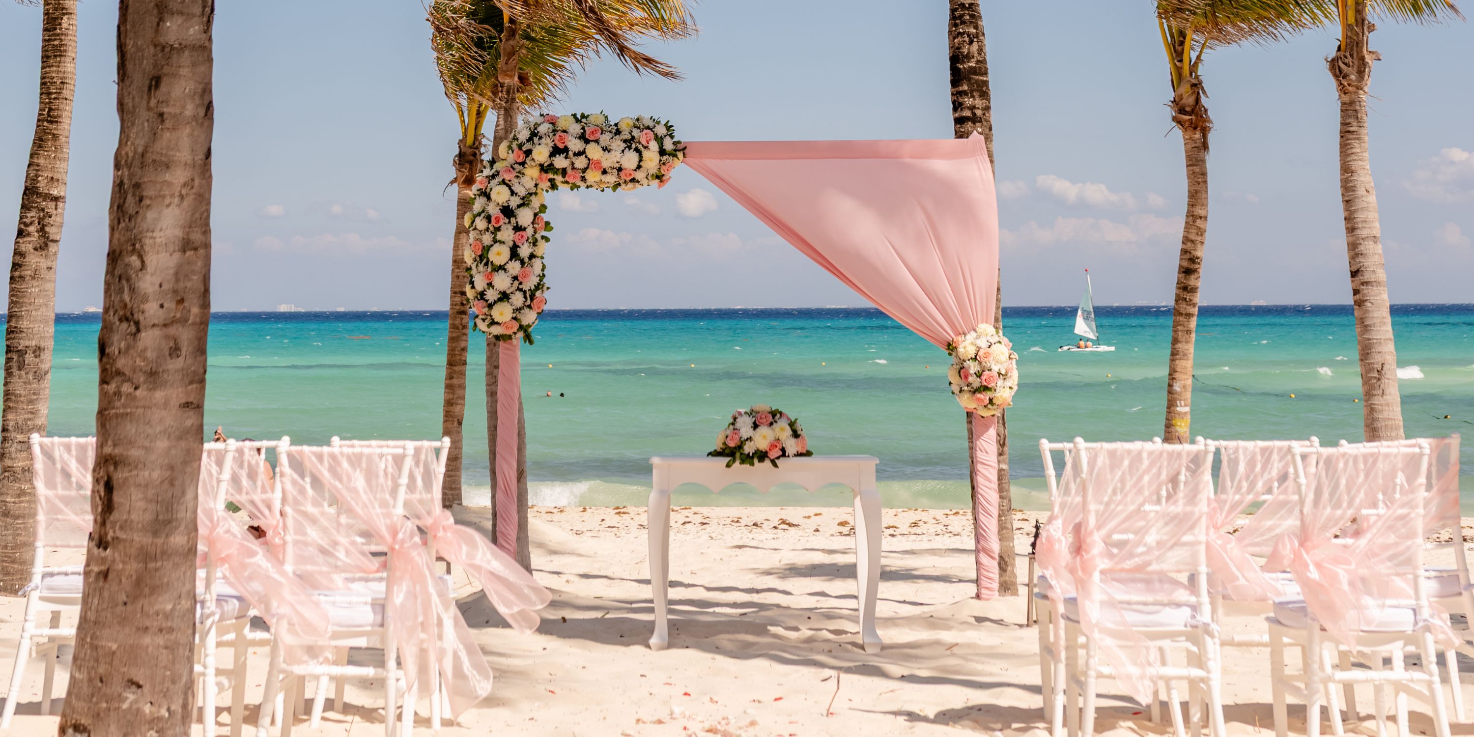 Destination wedding ceremony at Hotel Riu Palace Riviera Maya, featuring pink drapery, florals, and ocean views.