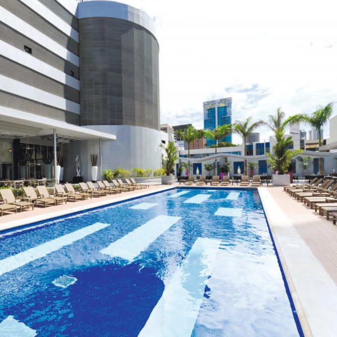 Hotel Riu Plaza Panama with lounge chairs at a modern hotel, ideal for a destination wedding, shadow of a building reflecting on water, clear sky.