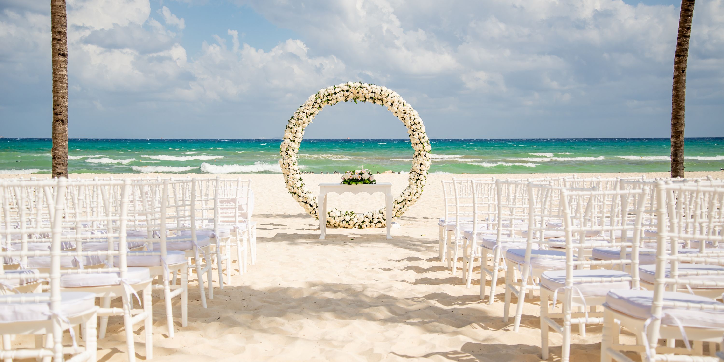 White chairs and a floral arch arranged on the beach for a destination wedding at Hotel Riu Yucatan.