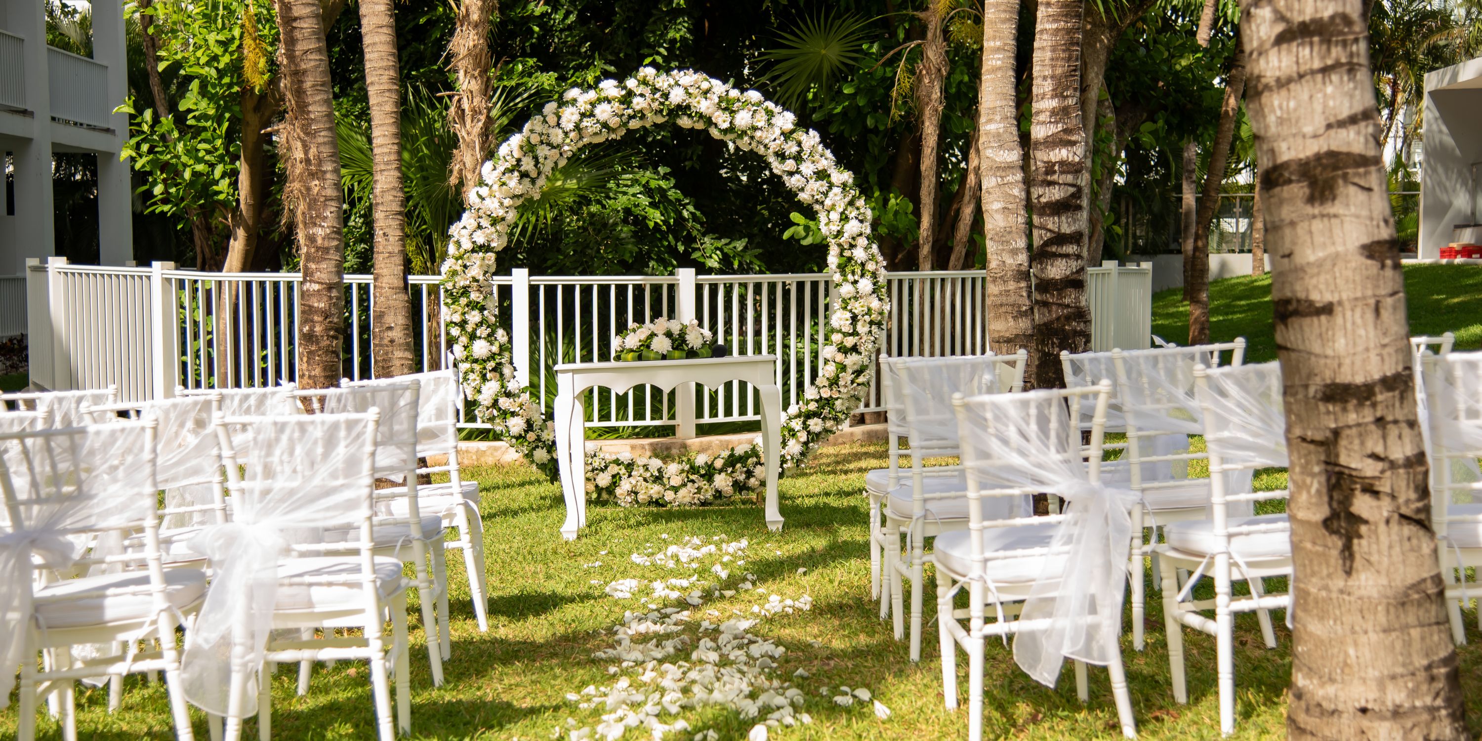 Hotel Riu Yucatan destination wedding: elegant outdoor setup with white chairs, floral arch, and petals.