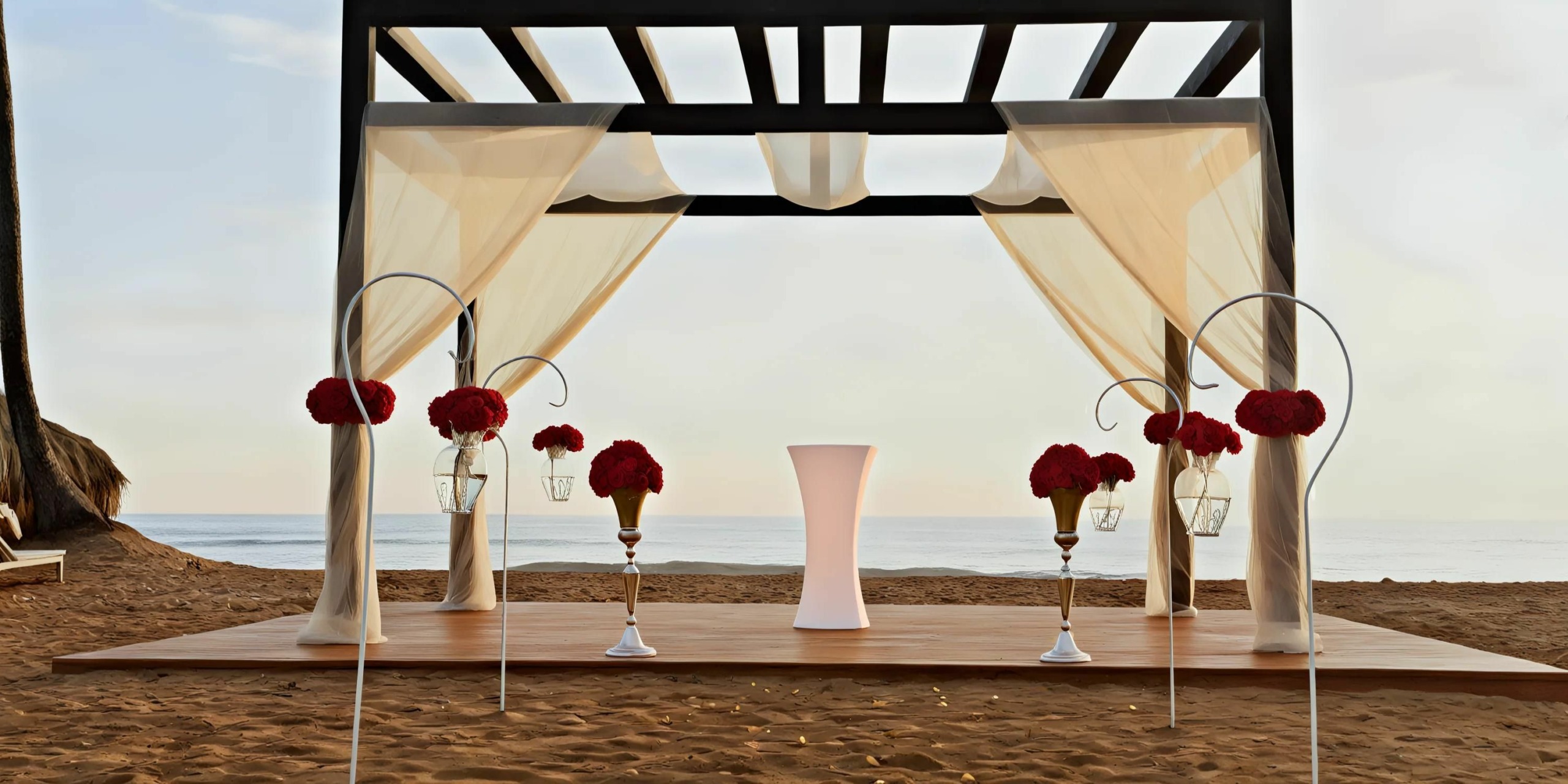 Outdoor beachside wedding altar with a black frame, white curtains, and red floral decorations. The altar features a central white pedestal on a wooden platform, with the ocean in the background.