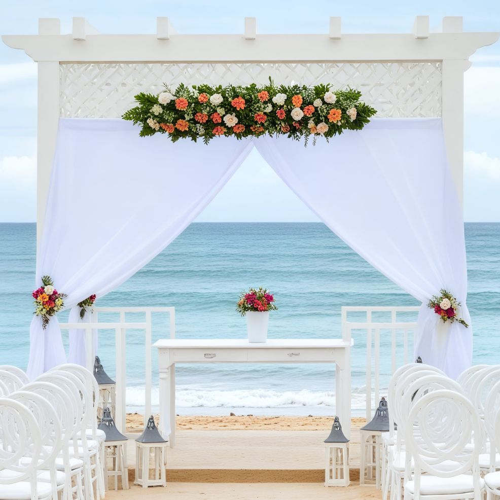 A stunning destination wedding arrangement featuring a floral arch and elegant white chairs overlooking the ocean.