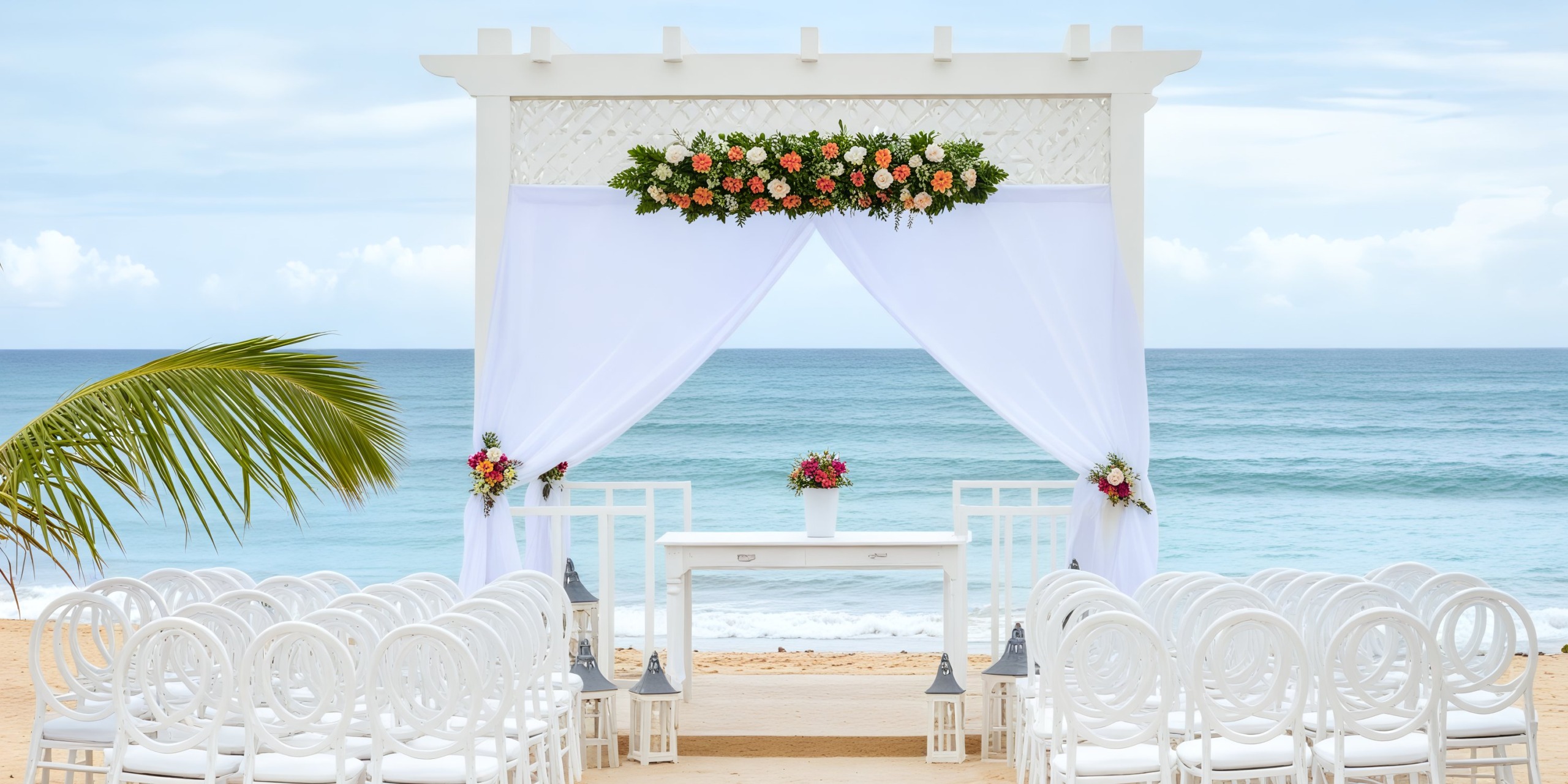 The setup for this destination wedding features an outdoor beach setting where rows of white chairs are arranged to face a beautifully decorated arch adorned with flowers.