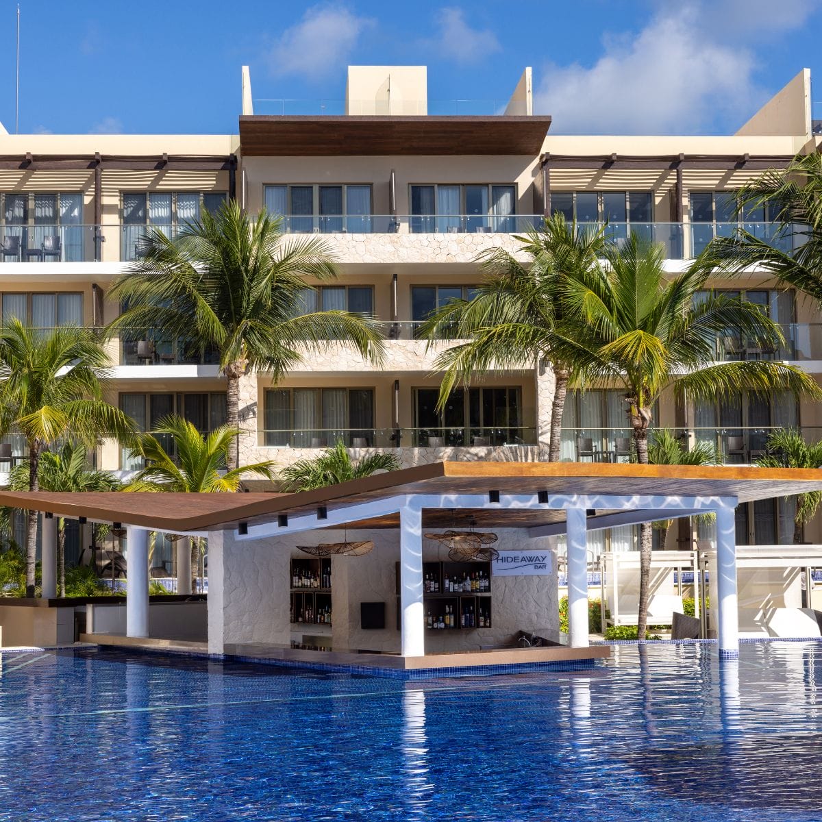 A poolside bar with palm trees at Royalton Hideaway Riviera Cancun, perfect for a destination wedding.