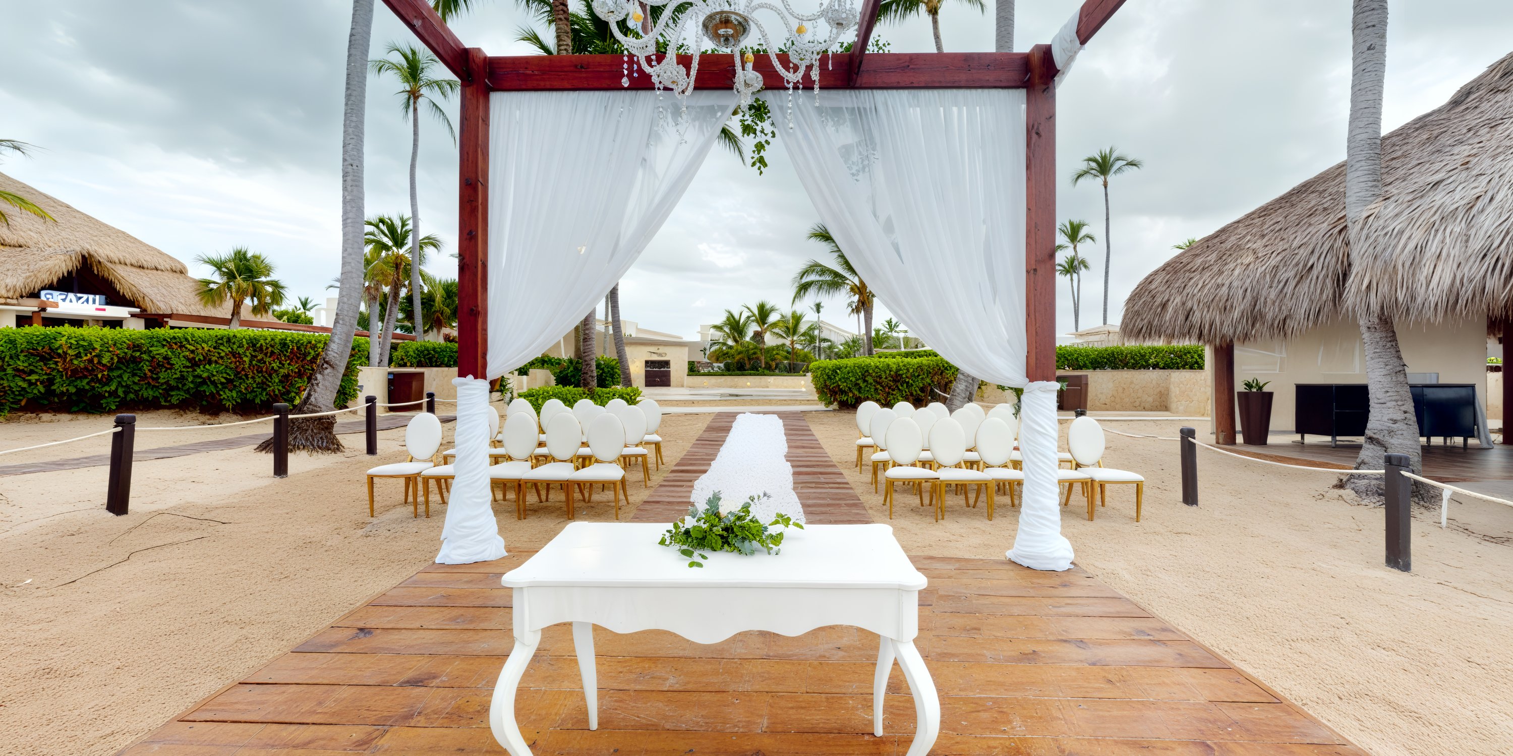 A picturesque destination wedding arrangement featuring white chairs, a beautifully draped canopy, and an elegant decorative chandelier overlooking the beachfront.