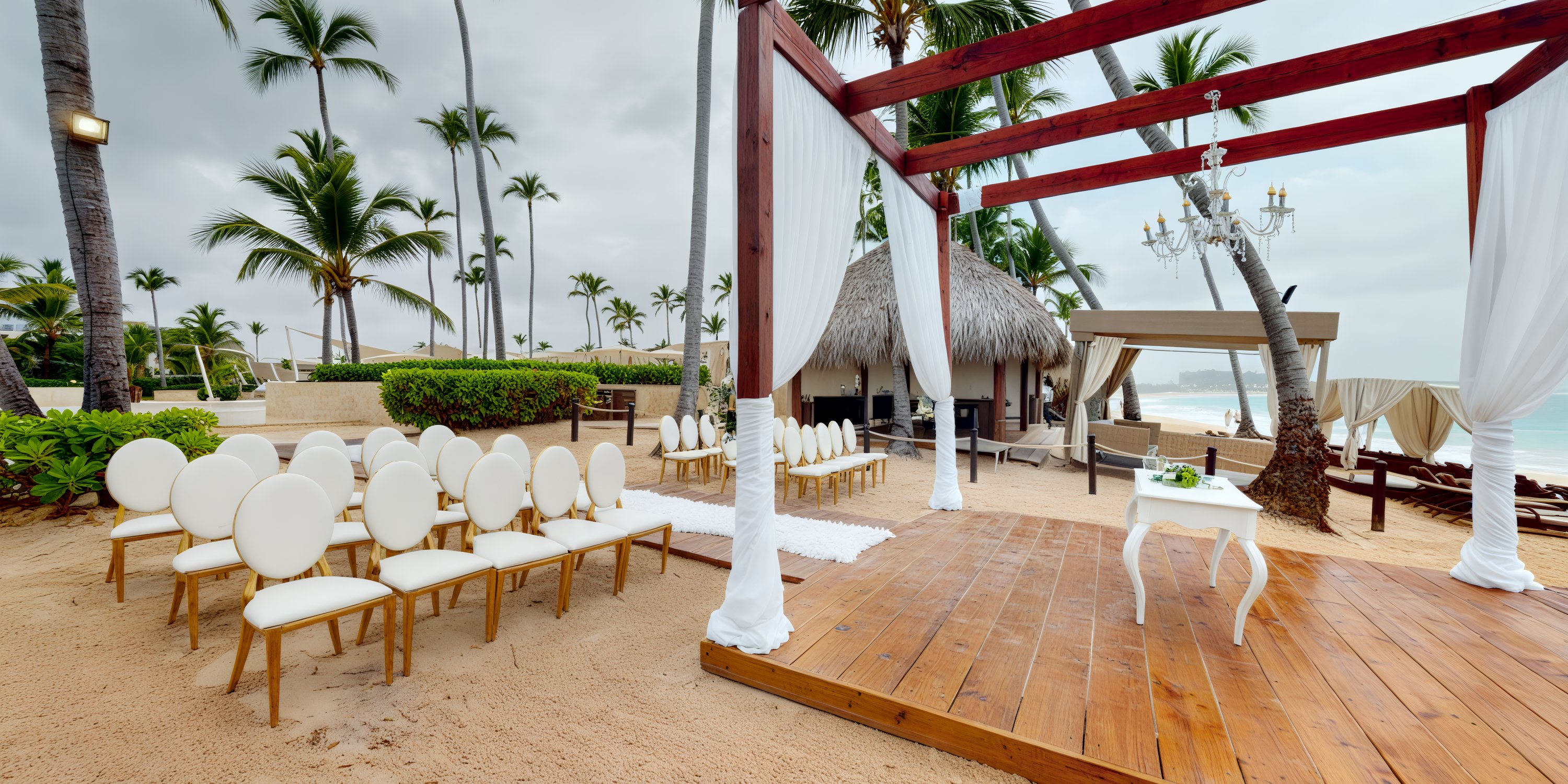 A destination wedding by the sea featuring a beautifully arranged beach setup with chairs, a wooden pergola, and breathtaking ocean views.