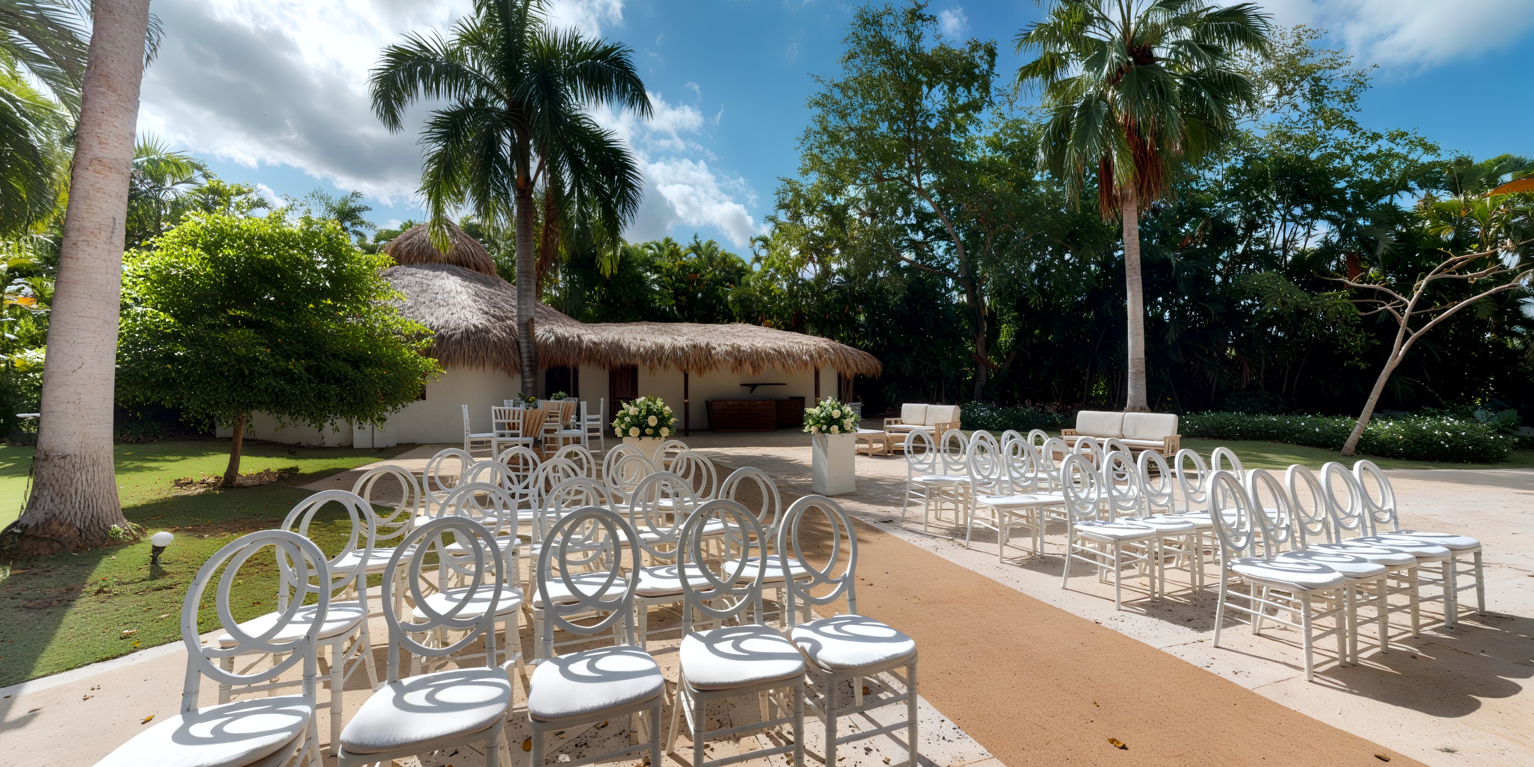 A stunning destination wedding location featuring white chairs, swaying palm trees, and a charming thatched-roof building.
