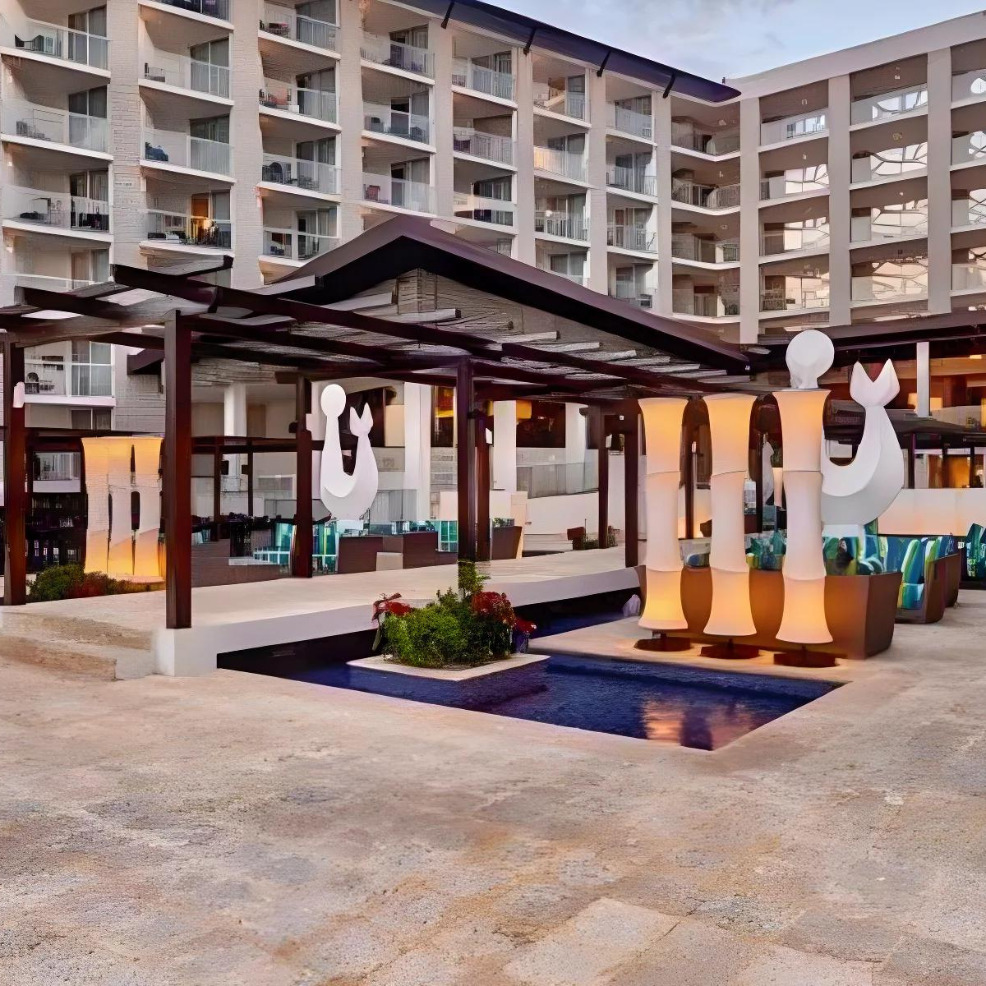 Modern hotel courtyard featuring a small pavilion with abstract sculptures, designed for destination weddings, surrounded by multi-story buildings with balconies.