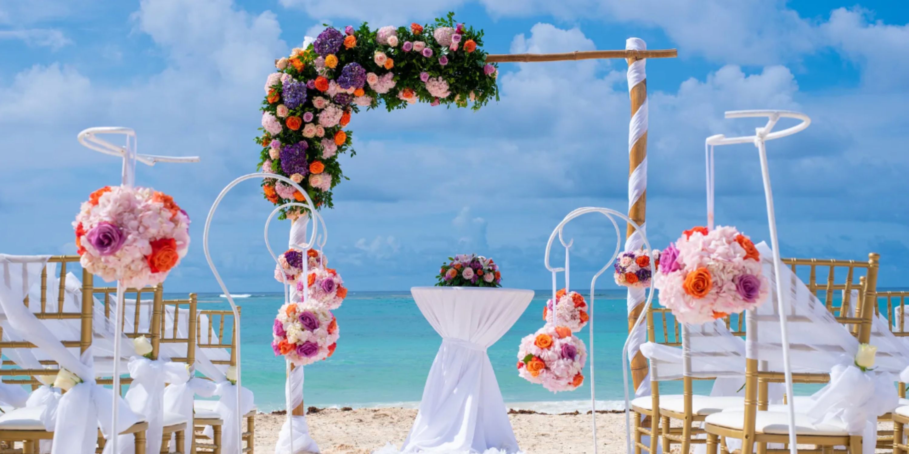 Destination wedding at Royalton Punta Cana with a floral arch, decorated chairs, and ocean backdrop.