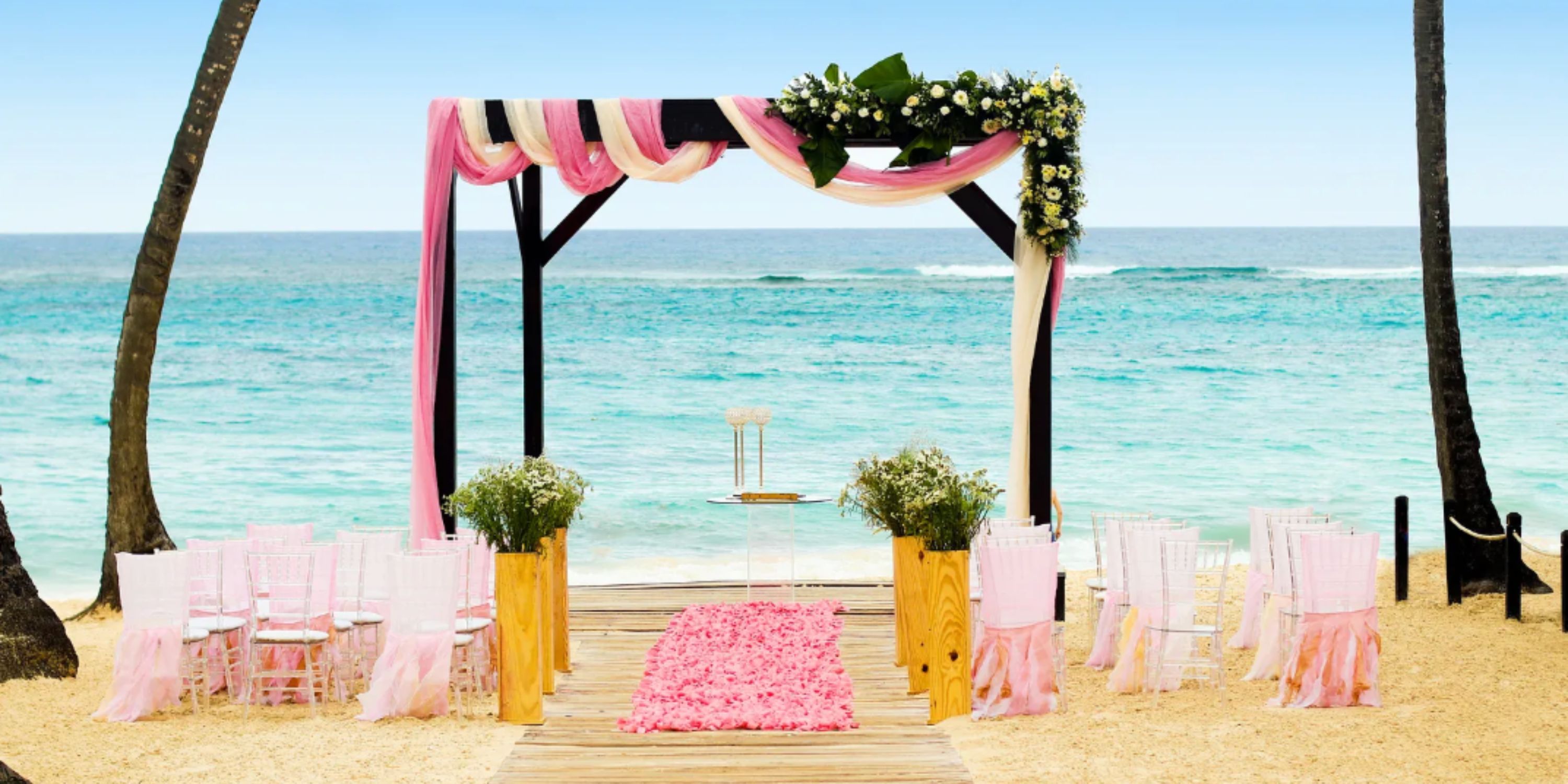 A destination wedding setup with a pink-draped arch and chairs on the beach at Royalton Punta Cana.