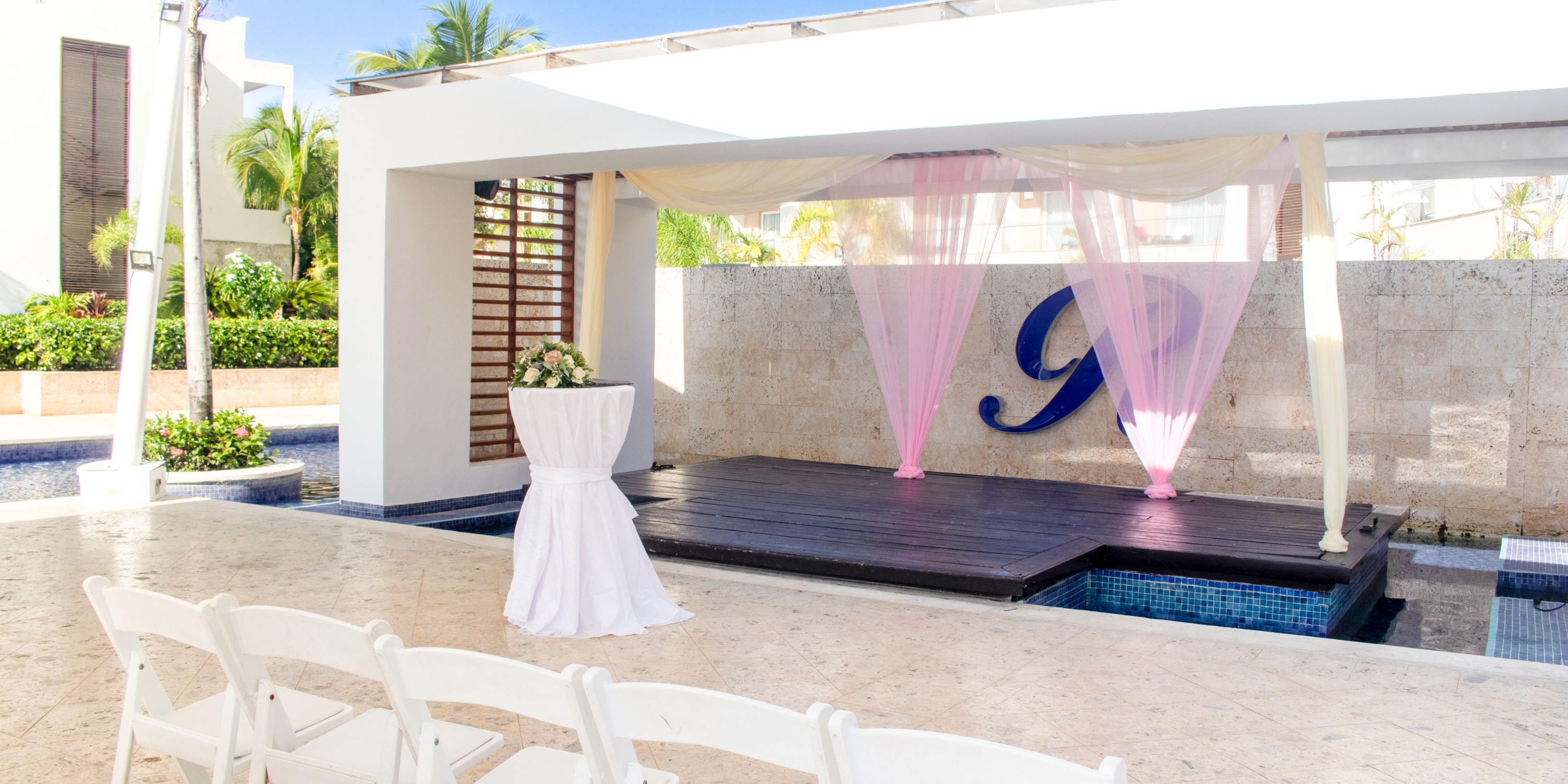 Destination wedding at Royalton Punta Cana featuring white chairs, floral accents, and pink stage drapery.