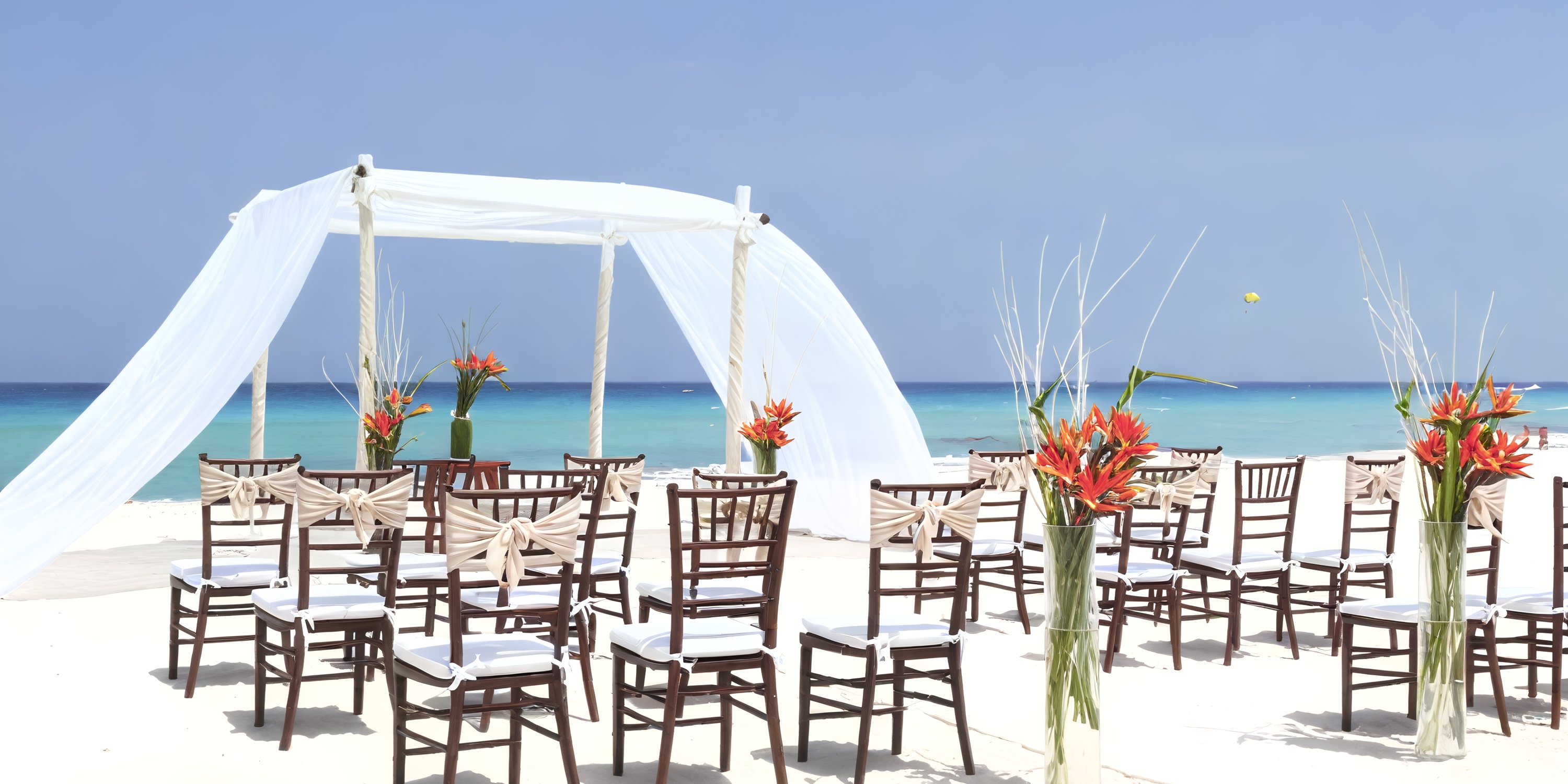 A destination wedding setup at Sandos Cancun Lifestyle Resort features a beautiful arrangement of chairs and a floral arch on the beach.