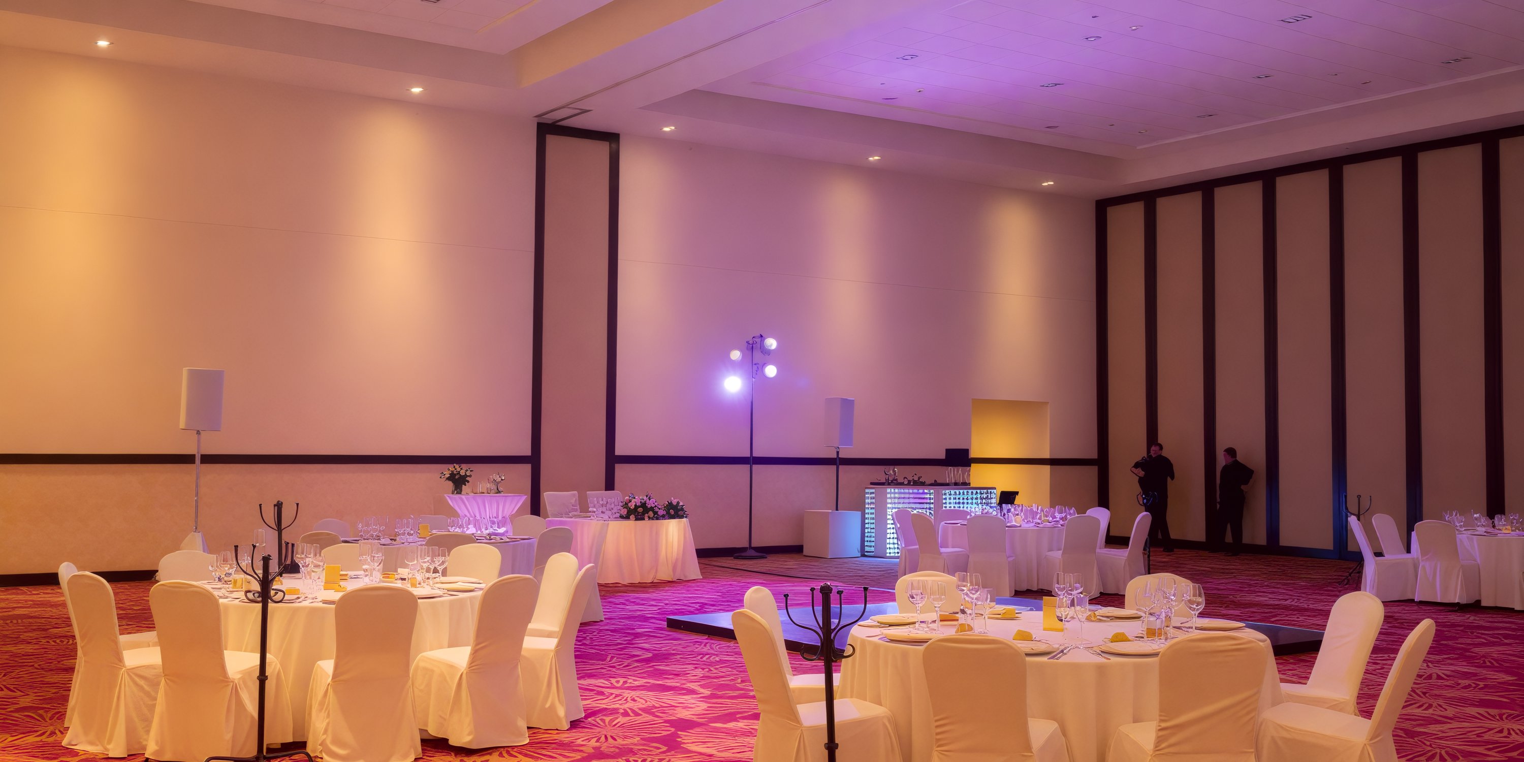 A vacant banquet hall at Secrets Vallarta Bay, elegantly set up for a wedding with round tables, white chairs, and stage lighting.