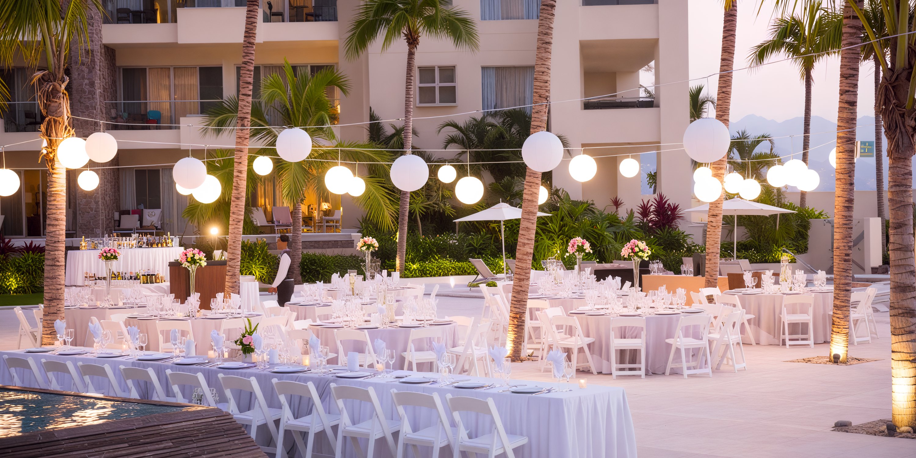 Secrets Vallarta Bay provides enchanting outdoor banquets, perfect for destination weddings, featuring elegantly arranged white tables and chairs, twinkling lights, and the natural beauty of palm trees.