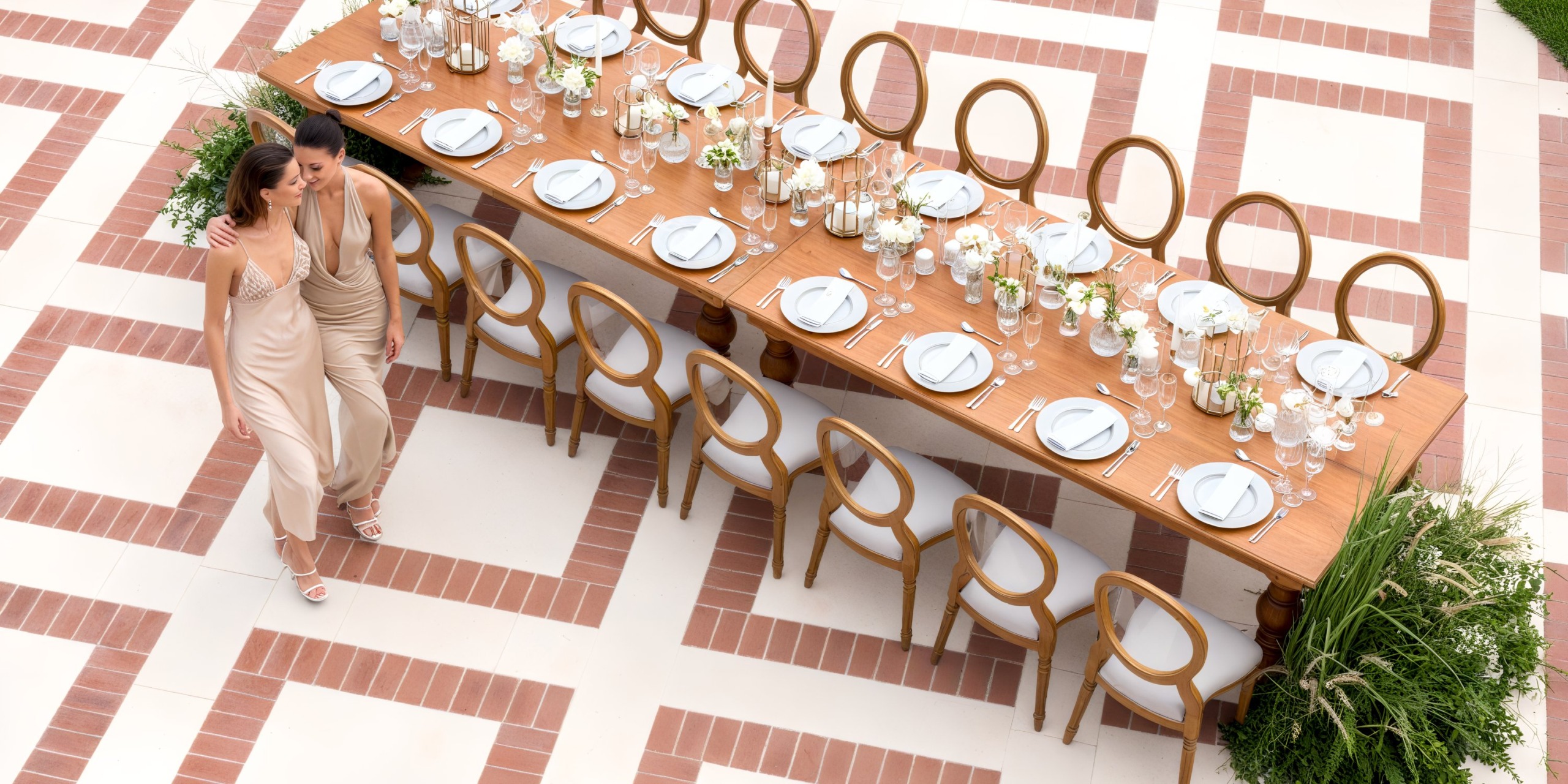 Two women stroll by a long, elegantly set dining table at Sanctuary Cap Cana, admiring the perfect setup for a destination wedding.
