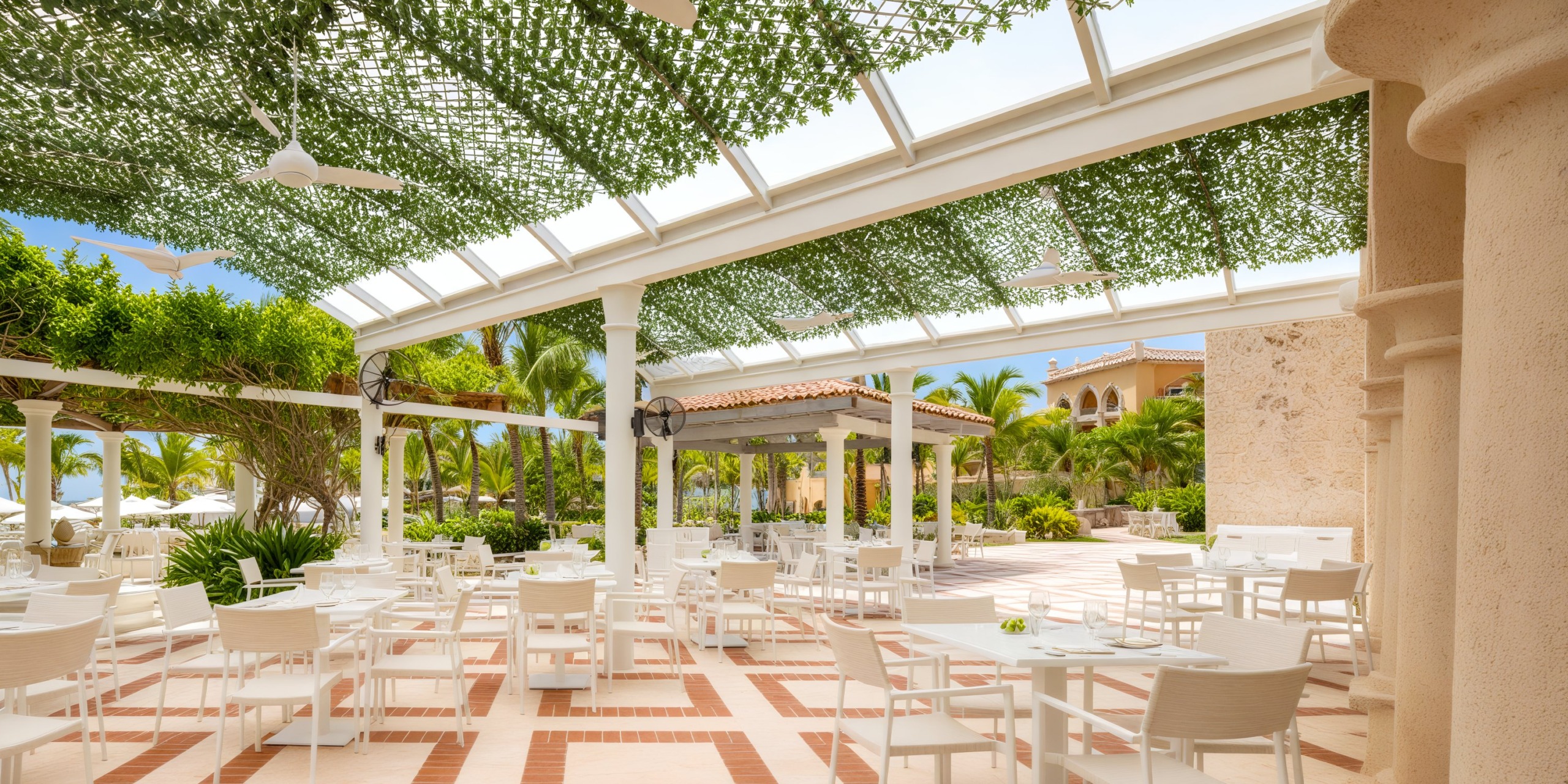 Sanctuary Cap Cana's outdoor patio, perfect for a destination wedding, showcases white tables and chairs nestled beneath vibrant, lush greenery.