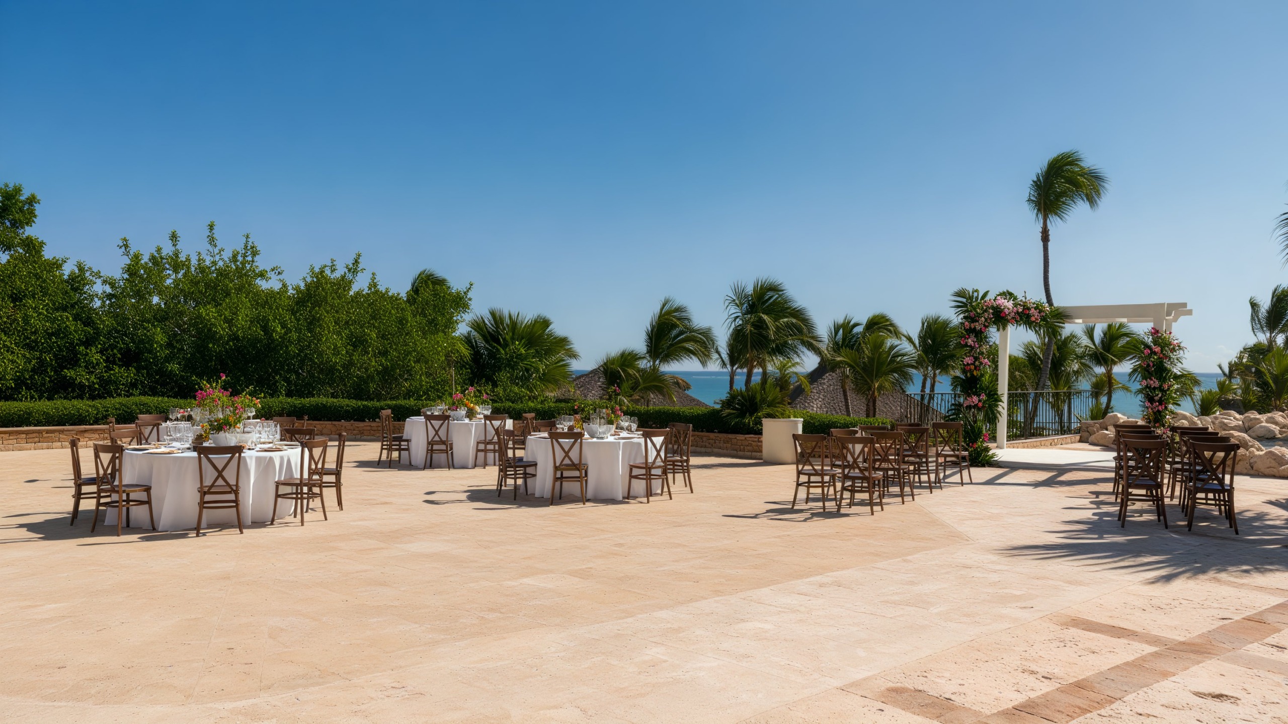 At Sanctuary Cap Cana, experience an exquisite destination wedding featuring round tables and chairs set by the ocean, complete with a stunning floral arch.