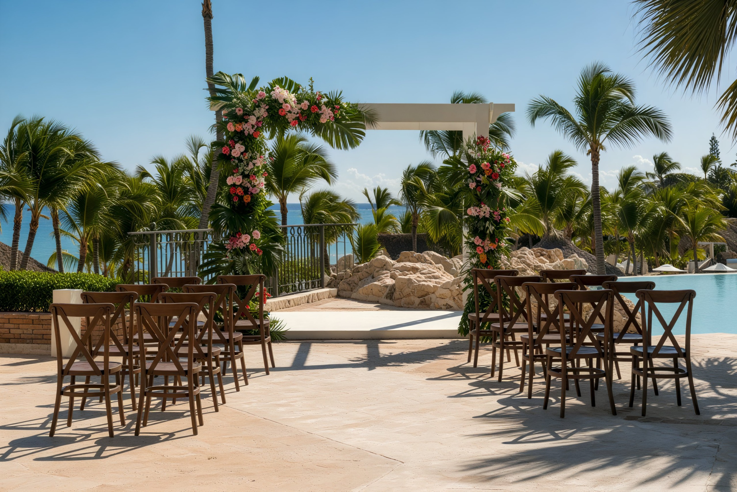 Sanctuary Cap Cana offers a stunning destination wedding setup featuring an outdoor arrangement by the pool, complete with elegantly placed chairs, a beautiful floral arch, and towering palm trees.