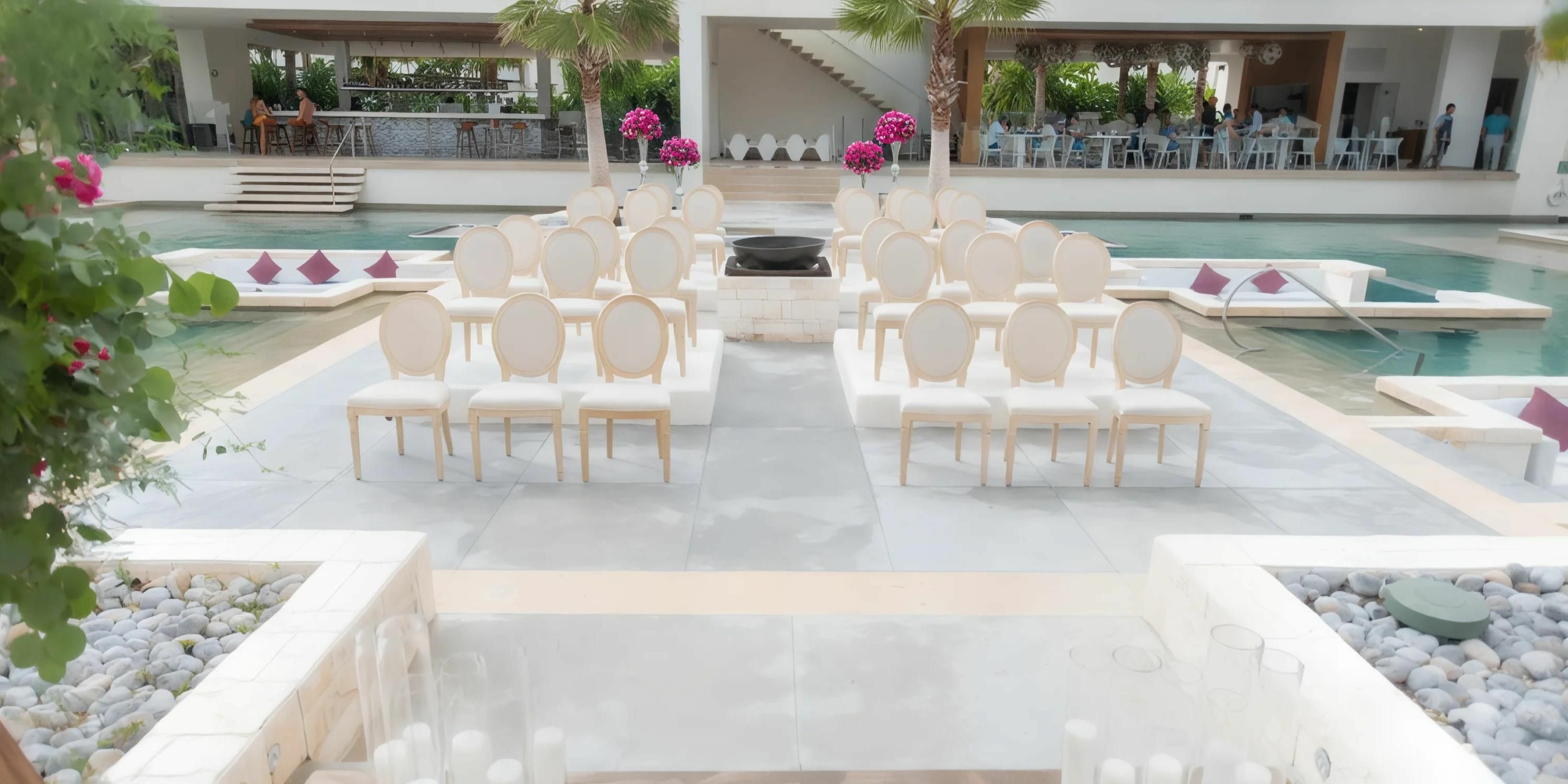 An outdoor wedding setup at Secrets Riviera Cancun features white cushioned chairs arranged in rows, a center aisle, and pink flower decorations. A pool is visible in the background along with a modern building.