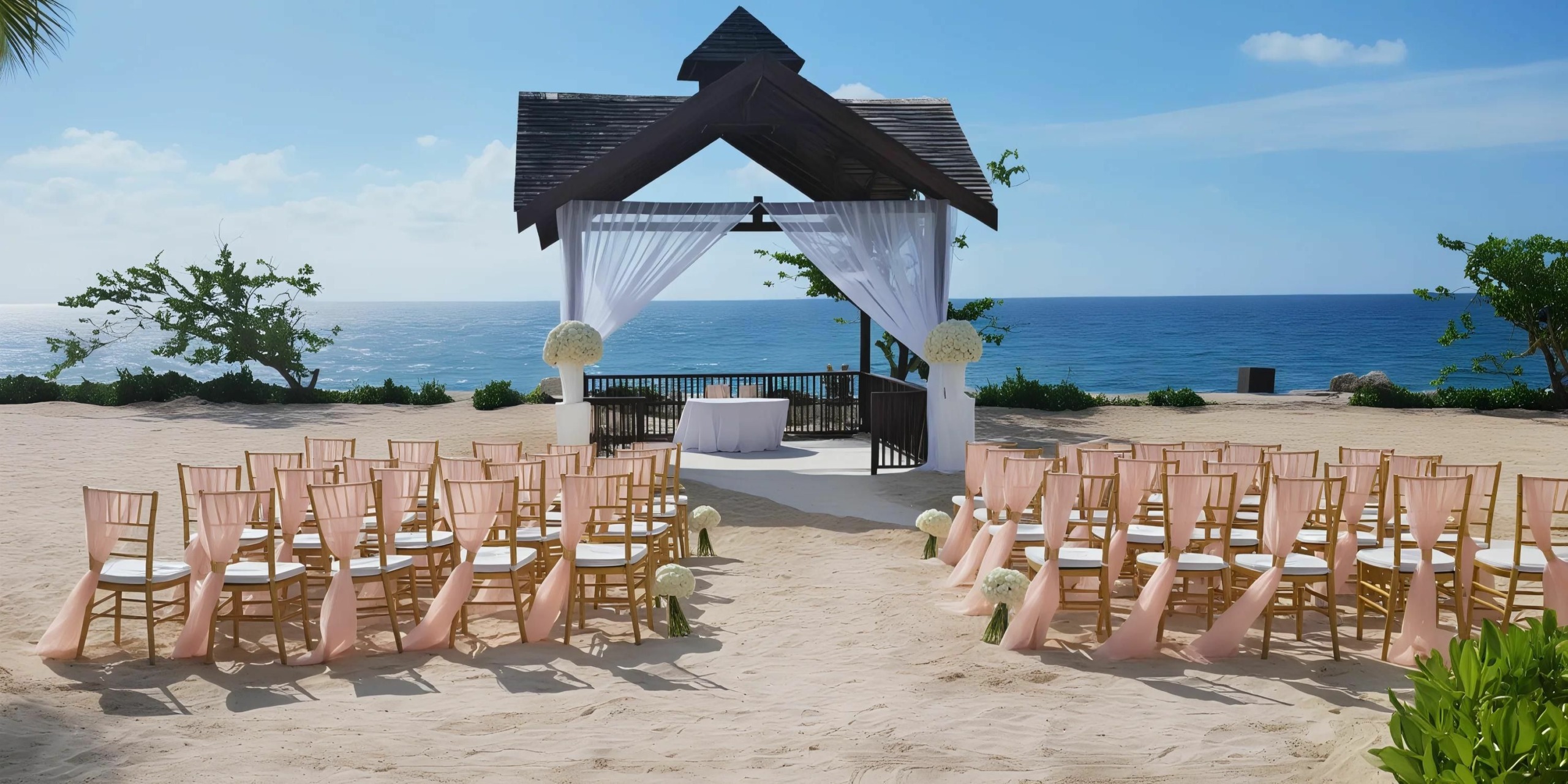 Outdoor beach wedding setup with a wooden arch and rows of chairs adorned with peach-colored fabric, facing an ocean view under a clear blue sky.