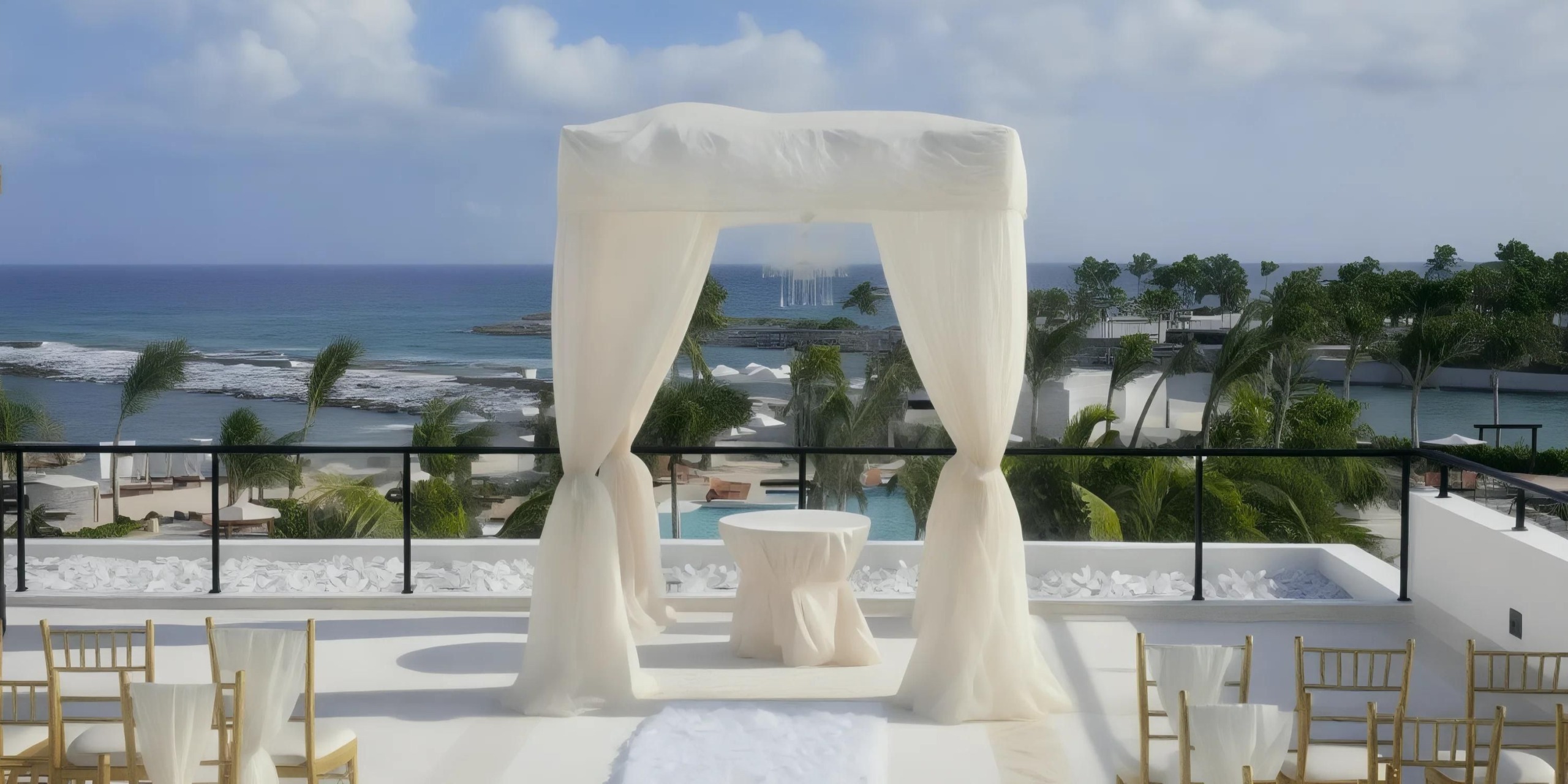 A white draped canopy set up for a wedding ceremony overlooks a beach and ocean. Rows of chairs are arranged on either side of an aisle leading to the canopy.