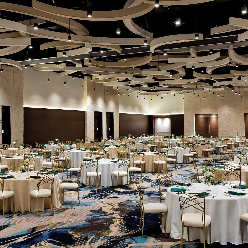 Elegant banquet hall designed for destination weddings, featuring intricate ceiling designs and modern decor with round tables set for an event.