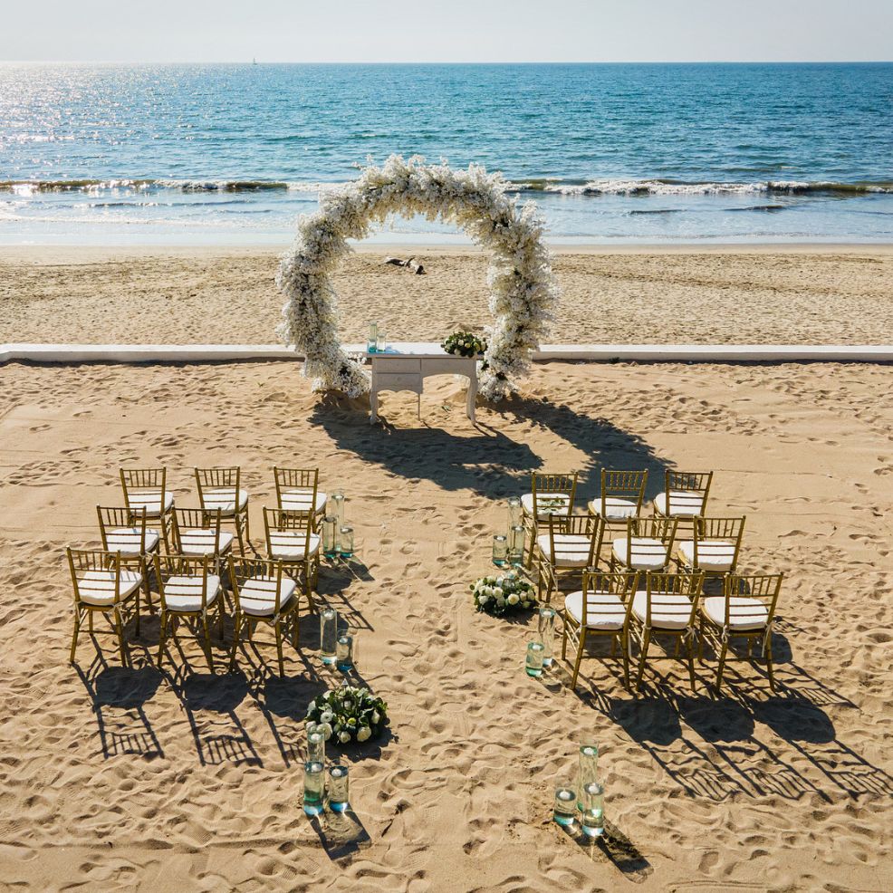 A destination wedding setup features elegantly arranged chairs and a stunning floral arch, all perfectly positioned to face the ocean.