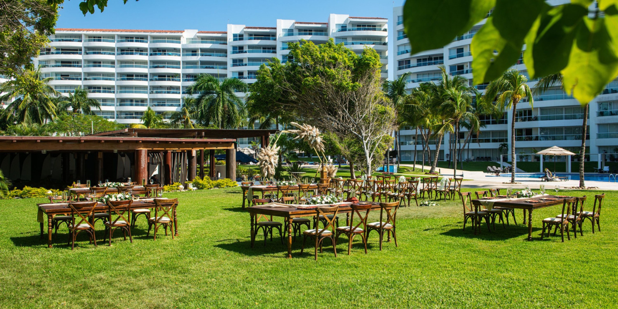 A picturesque outdoor wedding setup features elegant tables and chairs arranged on the lush grass, set against the backdrop of a grand white building.