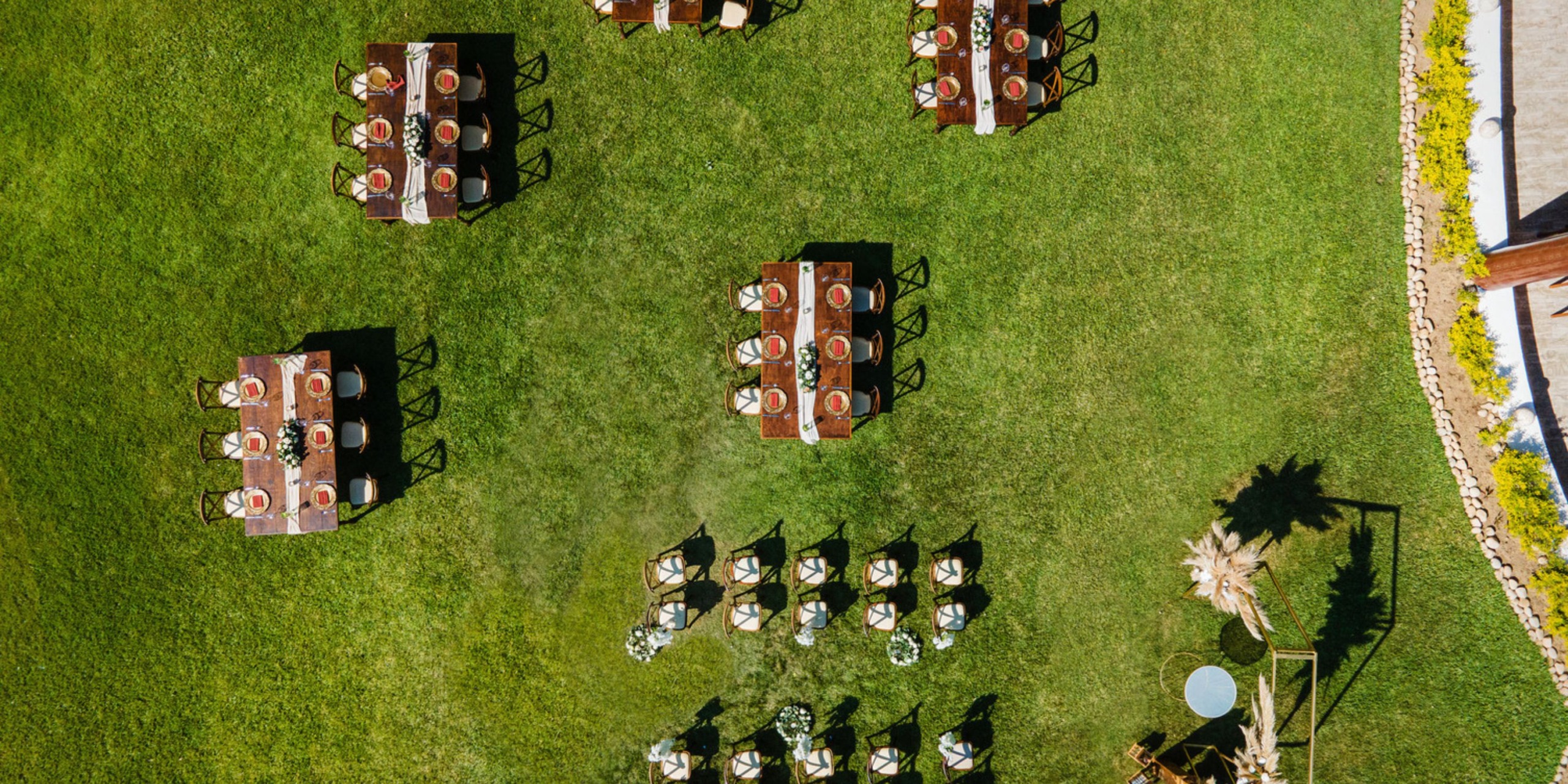 Aerial view of tables and chairs arranged on a lush green lawn, perfect for a destination wedding event.