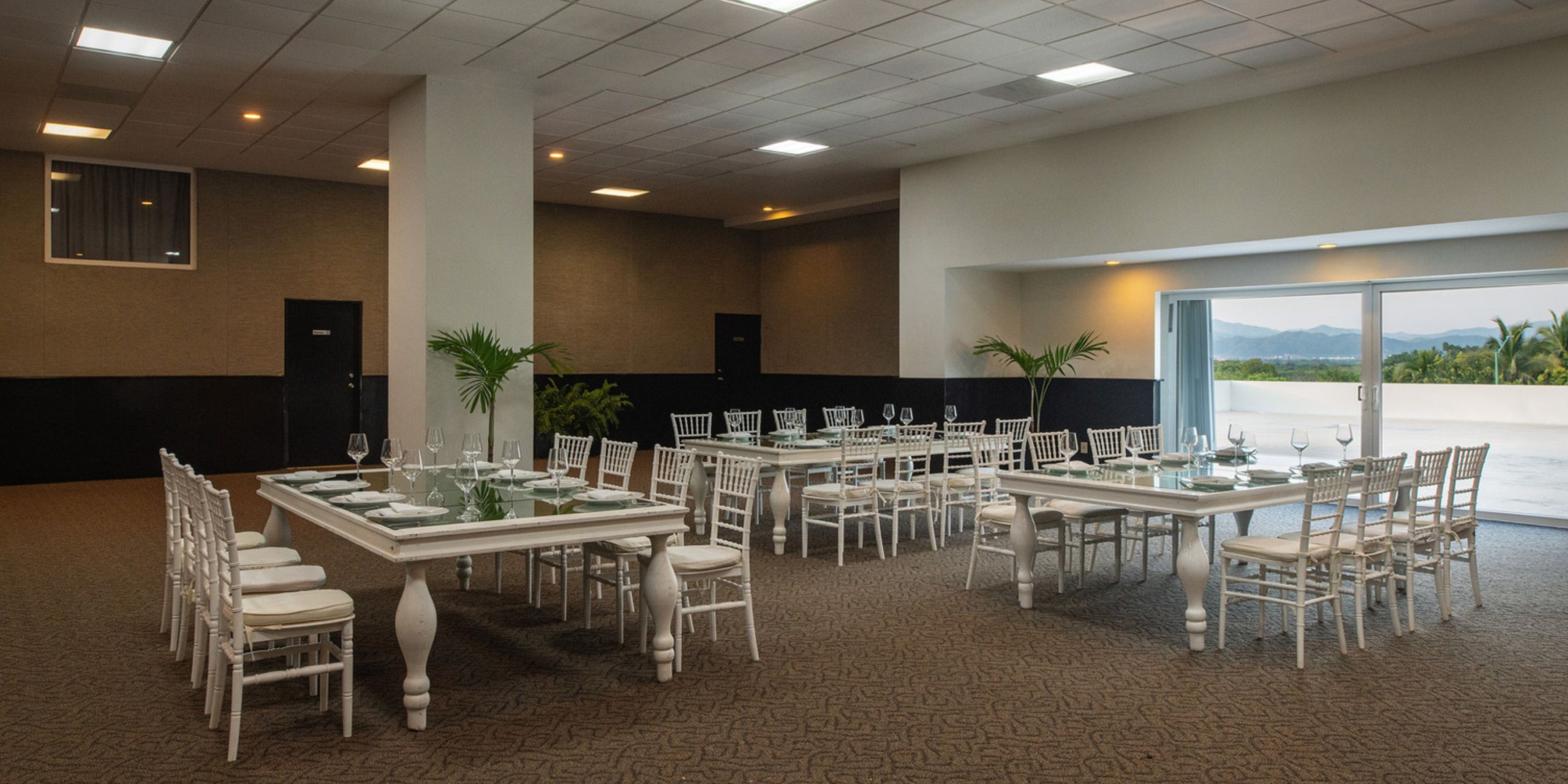 The spacious banquet hall at Wyndham Alltra Vallarta, adorned with two large white tables and chairs, is the perfect setting for a beautiful destination wedding.