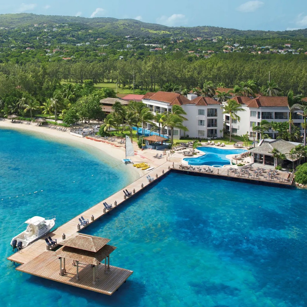 Aerial view of Zoetry Montego Bay, a tropical destination weddings resort with swimming pools, a sandy beach, and a dock extending into the clear blue ocean.
