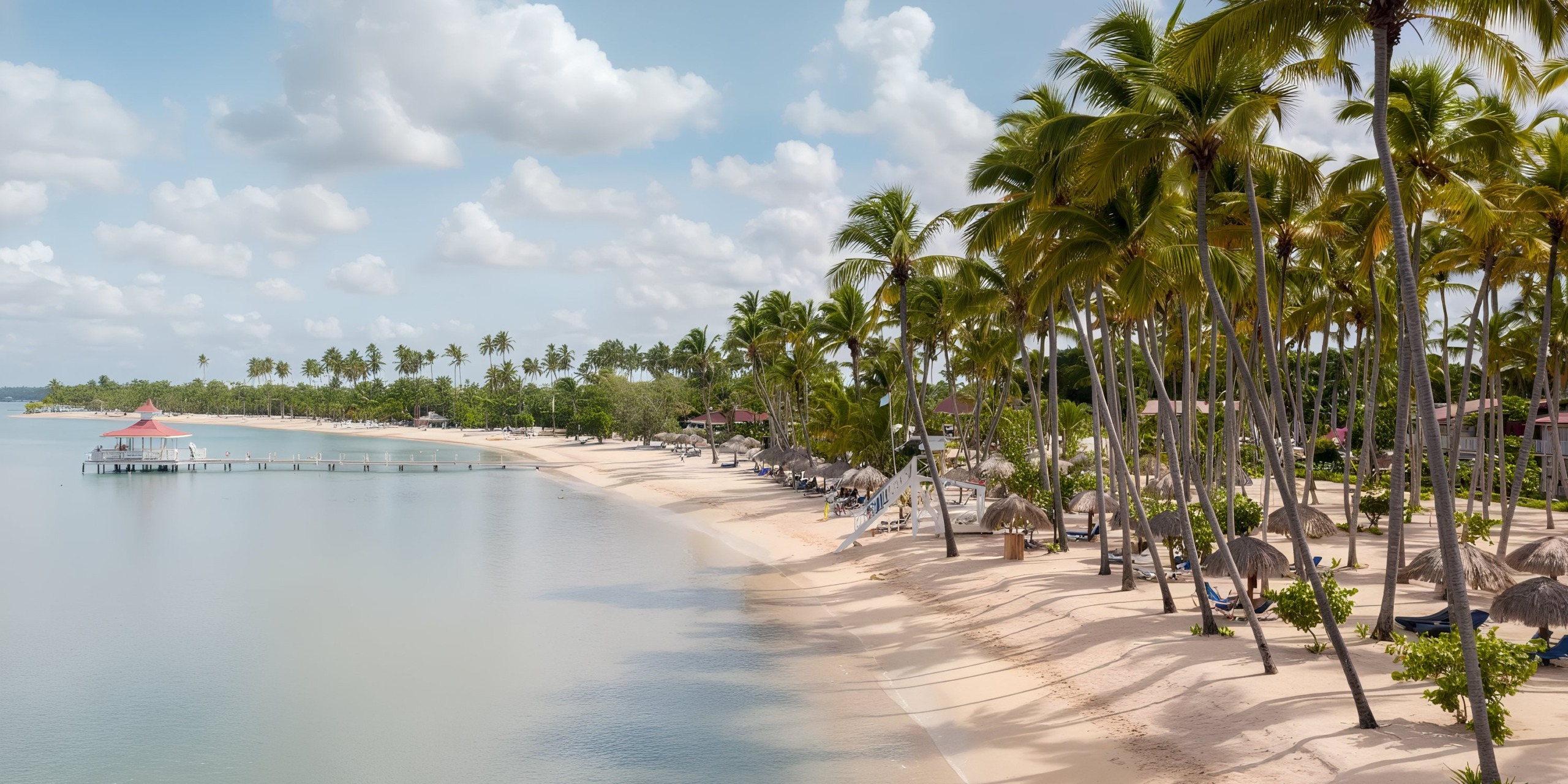 The tranquil setting of Bahia Principe Luxury Bouganville features a sandy beach lined with palm trees alongside calm, clear water beneath a partly cloudy sky. A pier reaches into the water, complemented by a small red-roofed structure.