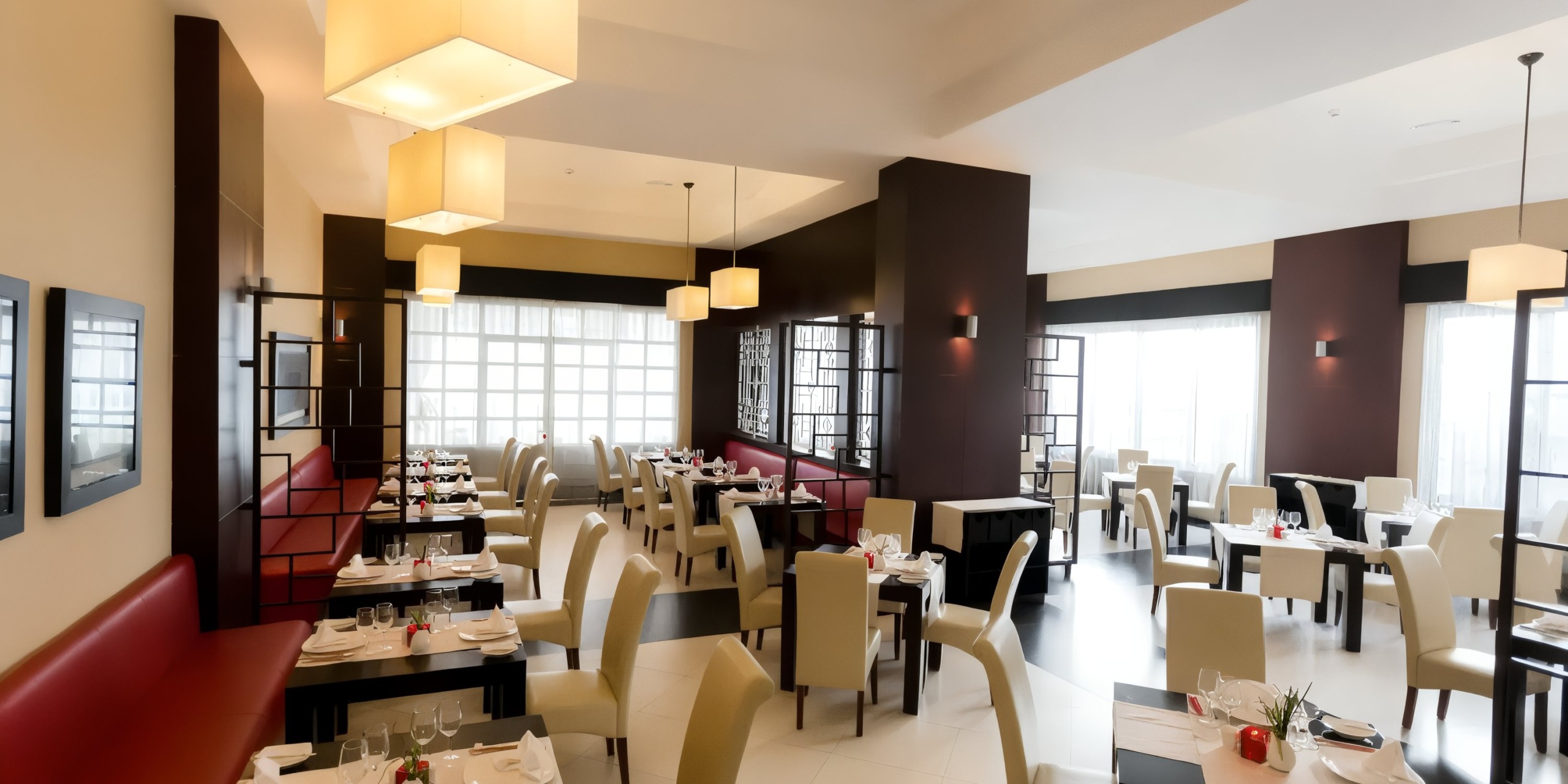 The interior of Bahia Principe Luxury Bouganville is modern, featuring cream-colored chairs, set tables, red booth seating, and large hanging light fixtures.