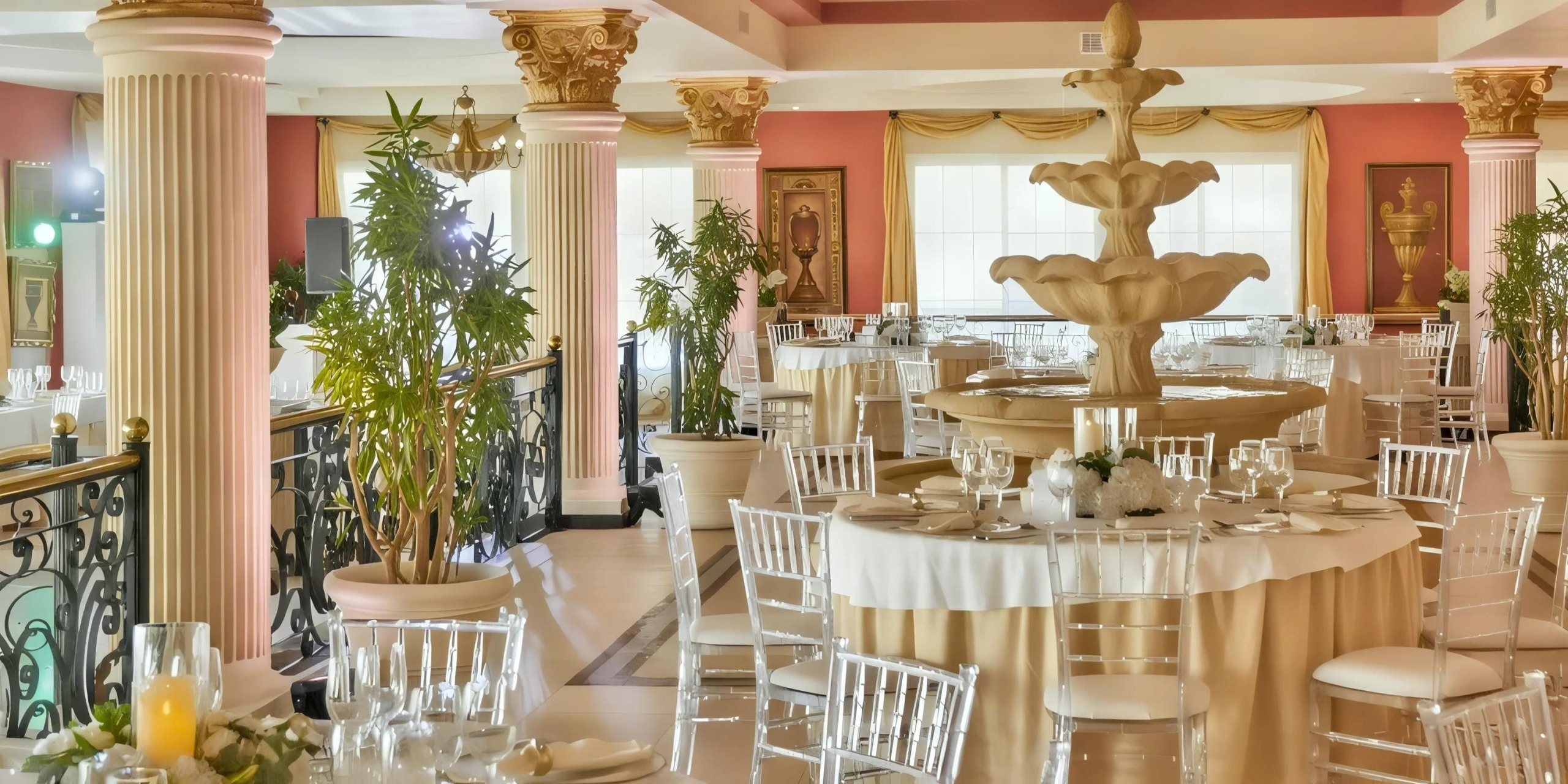 Elegant banquet hall with round tables, white table settings, large decorative fountain centerpiece, potted plants, and ornate columns.