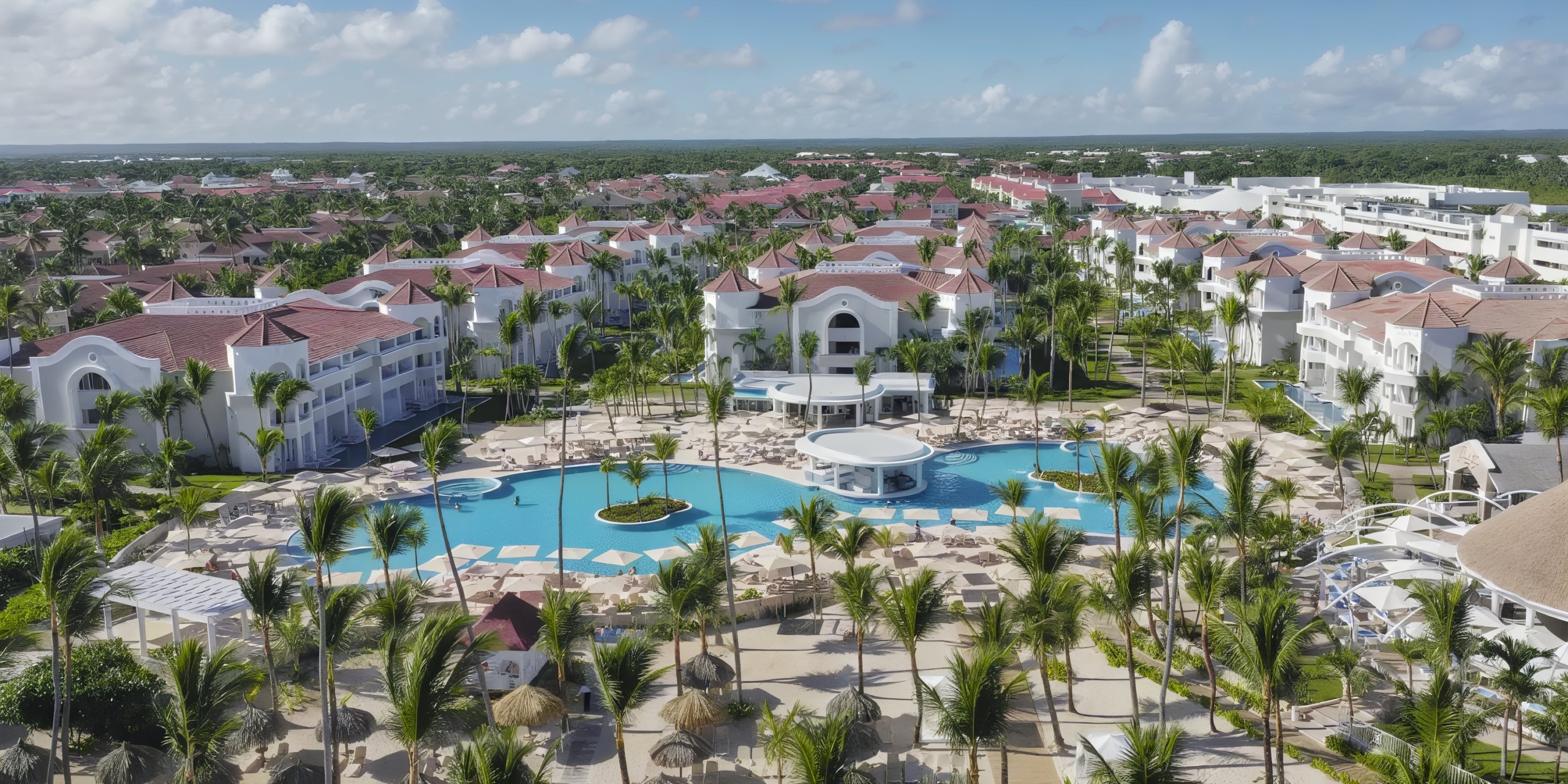 Aerial view of Bahia Principe Luxury Ambar resort with red-roofed buildings, a large central pool, and surrounding palm trees.