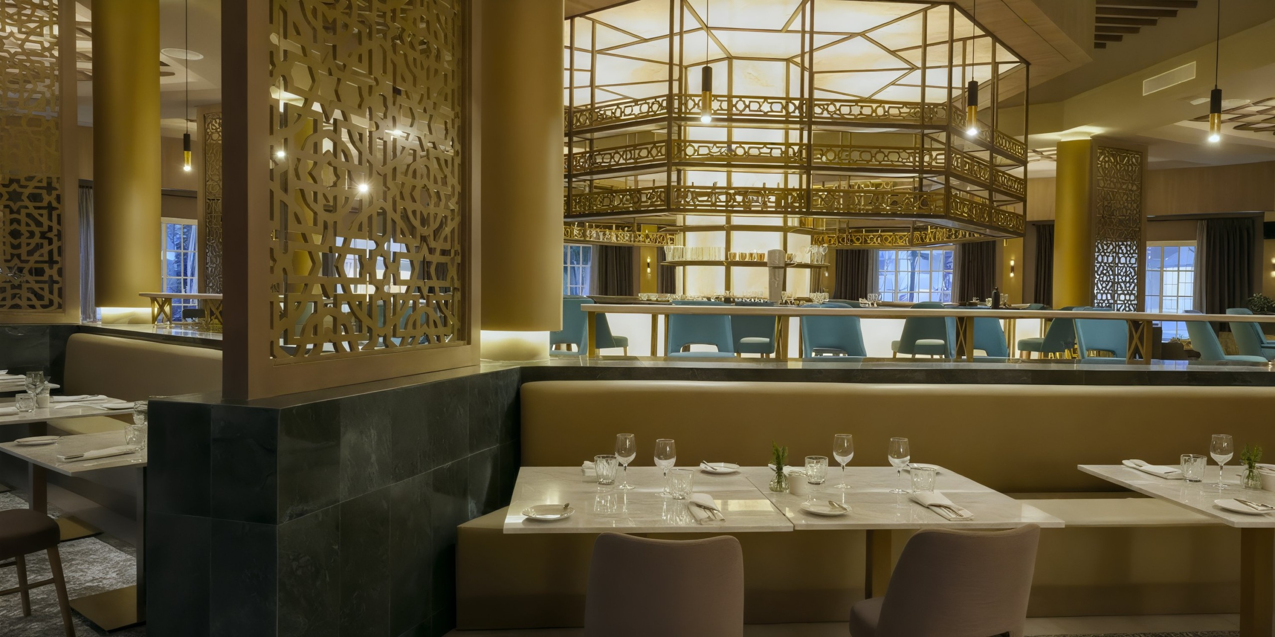 The Bahia Principe Luxury Ambar boasts a chic restaurant interior featuring decorative paneling, elegant lighting, and impeccably set tables adorned with glassware and cutlery.