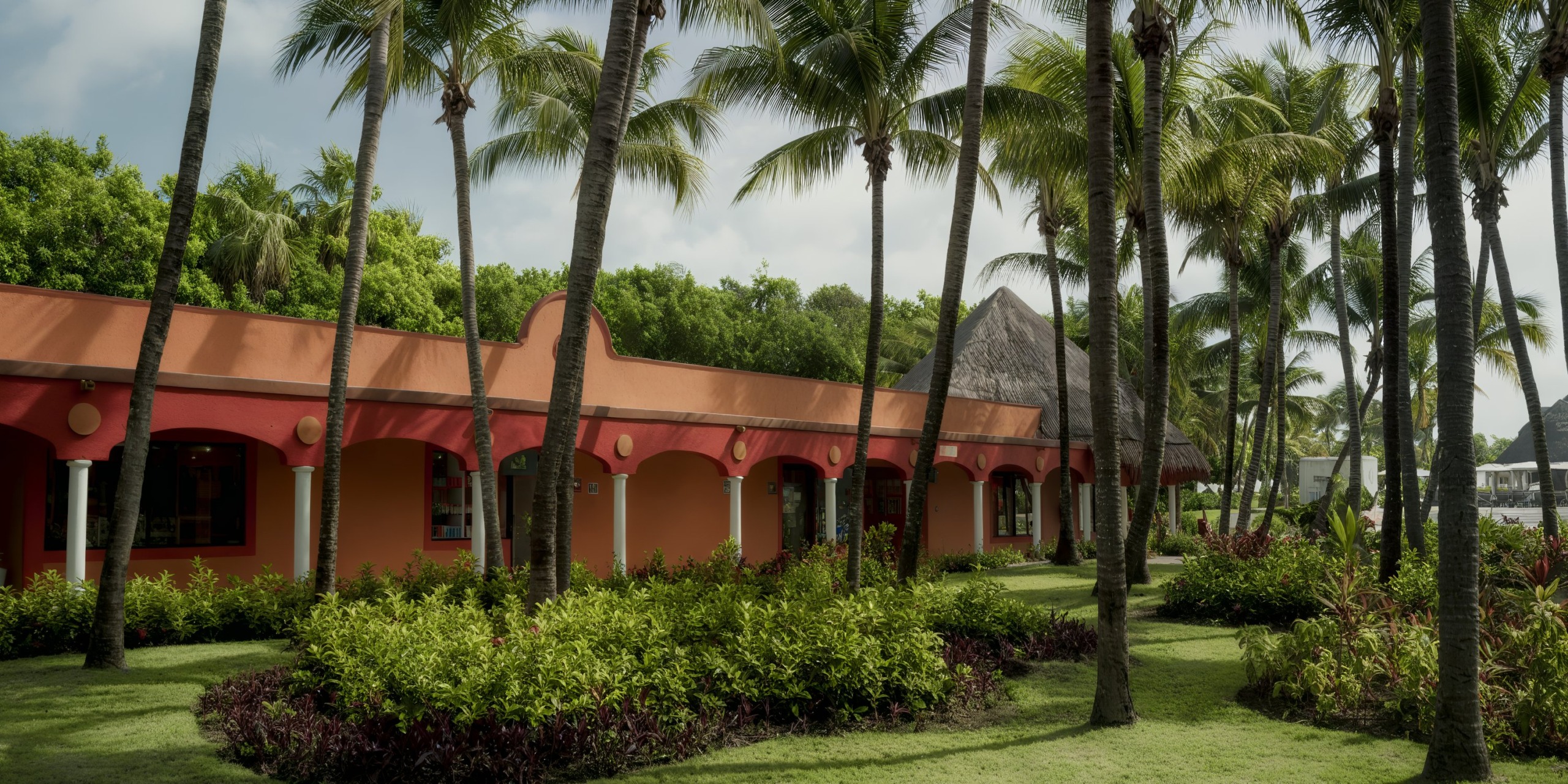 Catalonia Playa Maroma is an orange stucco building with arched openings, surrounded by palm trees and lush green landscaping.