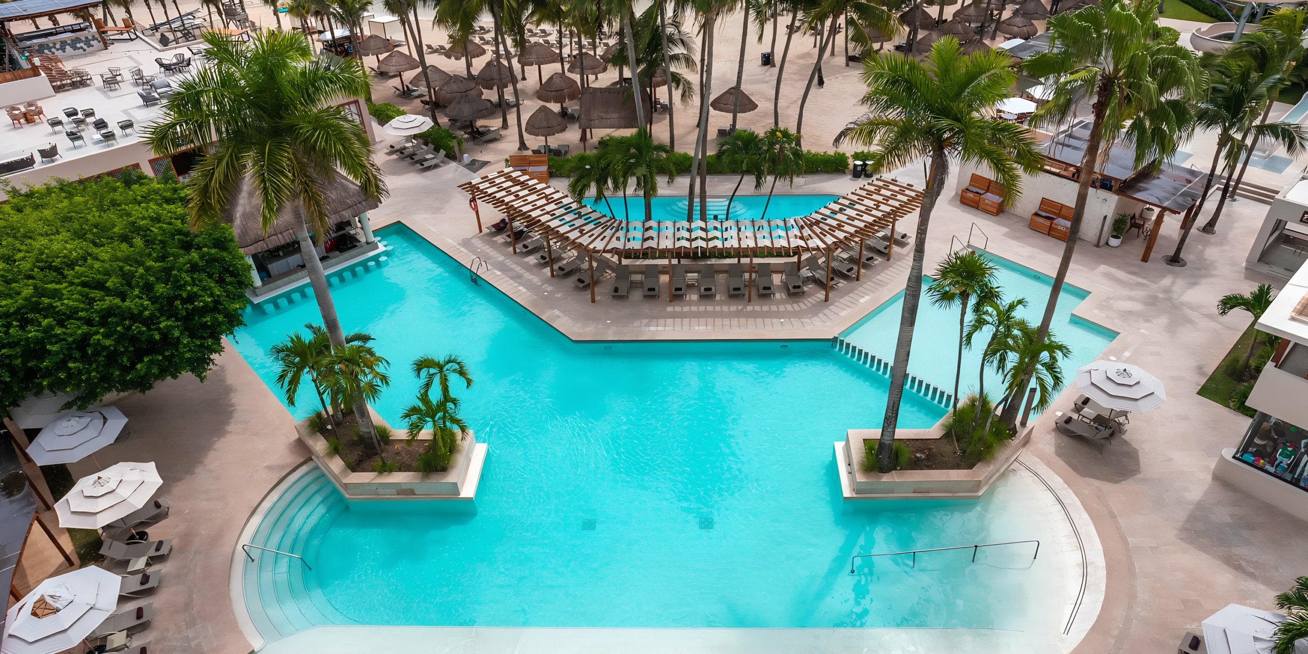 Aerial view of the Dreams Aventuras Riviera Maya resort swimming pool surrounded by lounge chairs and palm trees.