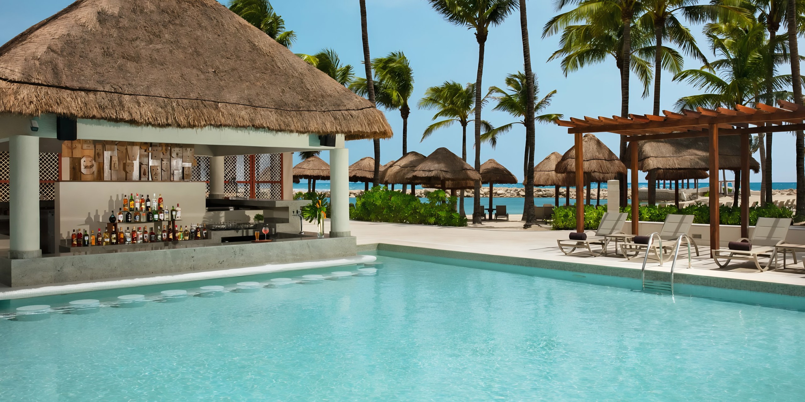 Dreams Aventuras Riviera Maya resort with palm trees and thatched umbrellas in the background.
