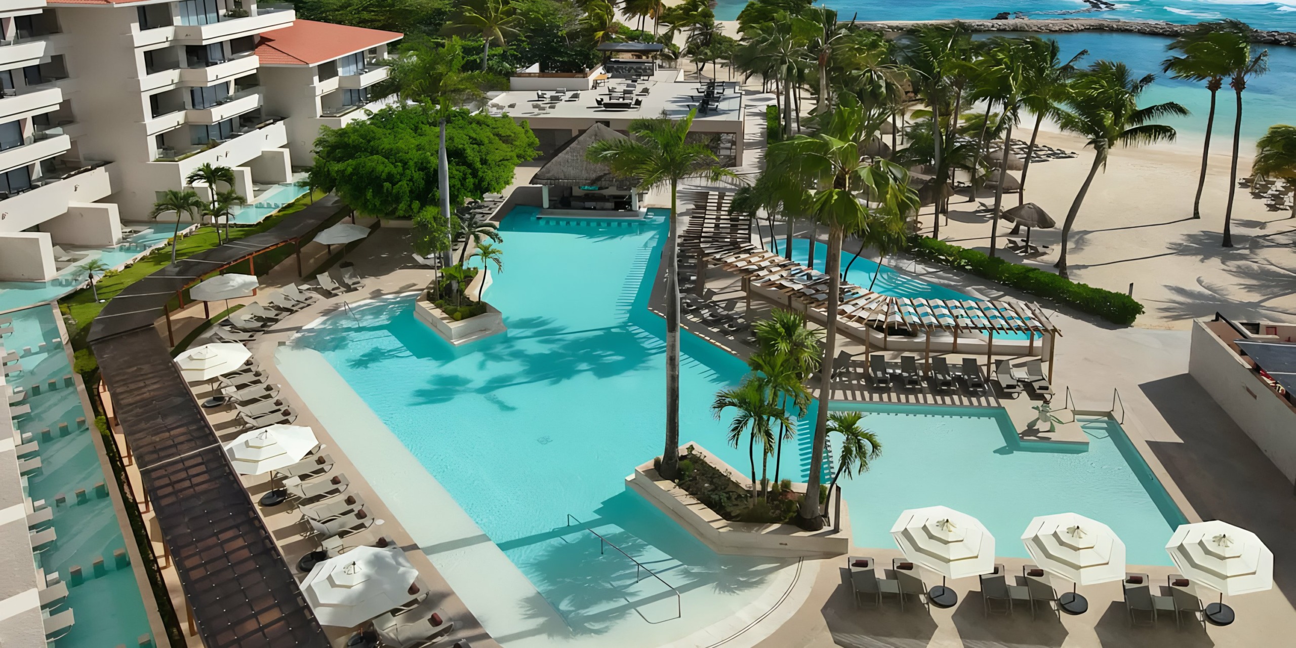 Aerial view of Dreams Aventuras Riviera Maya resort pool area by the beach with sun loungers and palm trees.