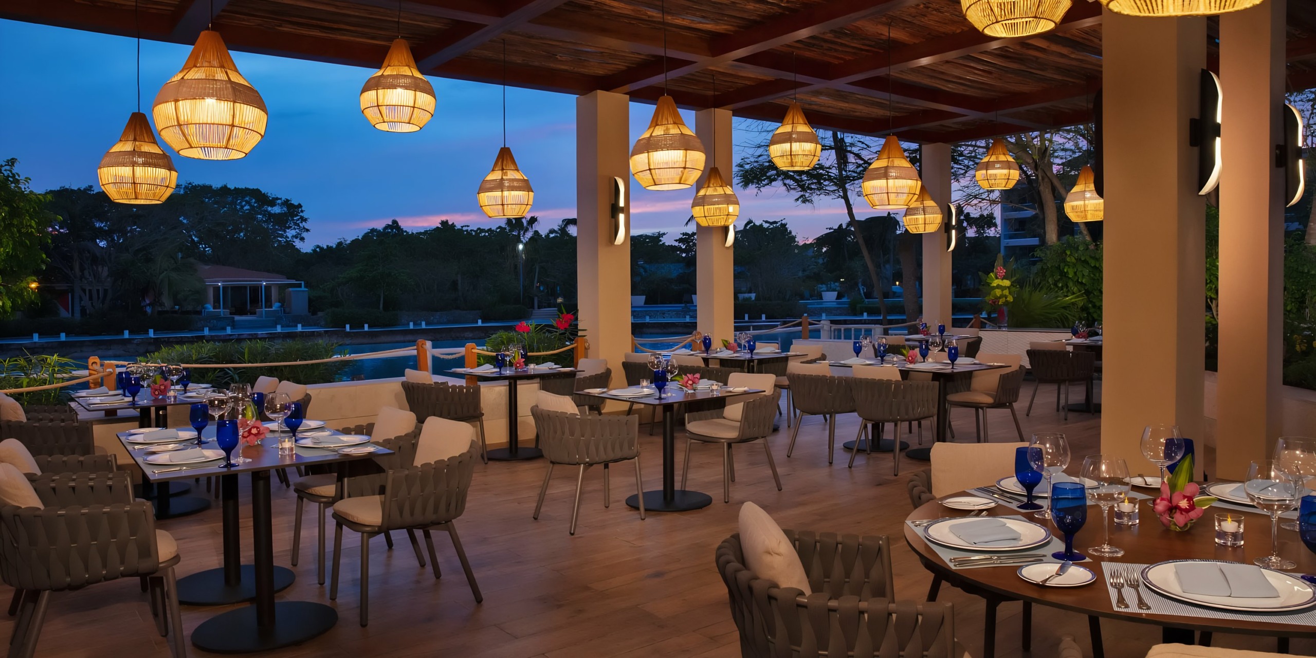 An elegantly set Dreams Aventuras Riviera Maya outdoor dining area with hanging lanterns at dusk.