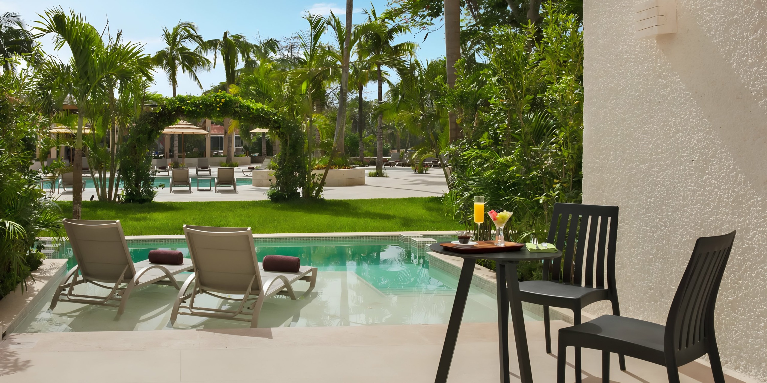 Dreams Aventuras Riviera Maya poolside relaxation area with loungers, tropical landscaping, and a small table with refreshments.
