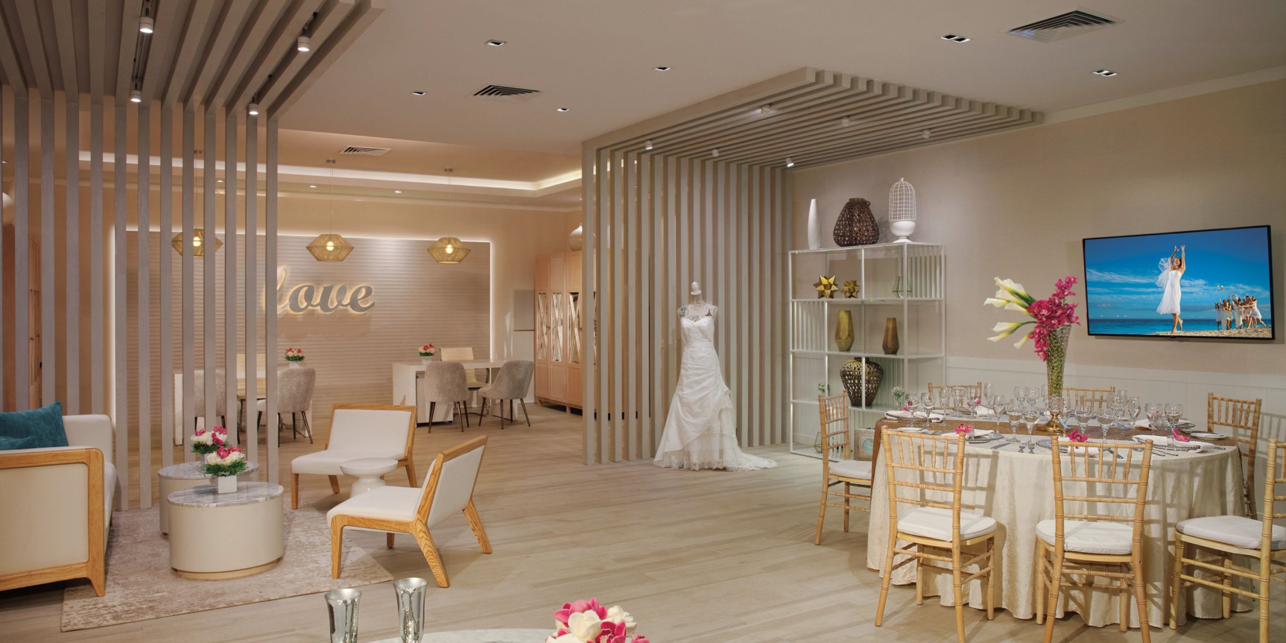 At Dreams Jade Riviera Cancun, the elegant event room features a beautifully set dining table, a wedding dress on display, and a "love" sign on the wall. The neutral tones and modern decor contribute to a sophisticated atmosphere.