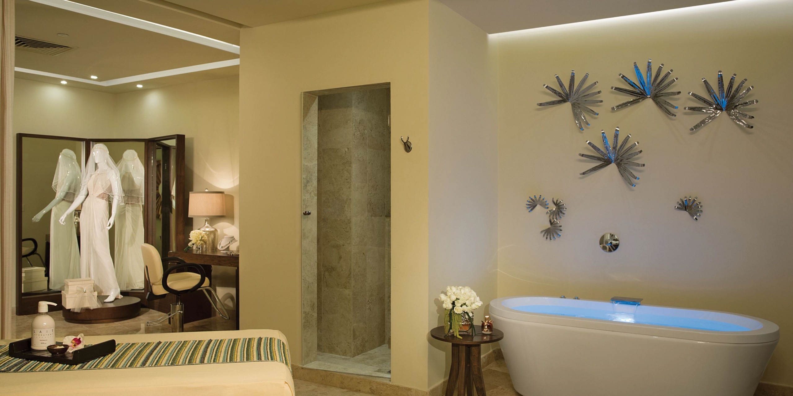 Experience the luxurious Dreams Jade Riviera Cancun spa room, featuring a modern bathtub, exquisite decorative wall art, a comfortable massage table, and an elegant mirrored vanity area. The ambience is enhanced with soft lighting and neatly arranged towels for your relaxation.