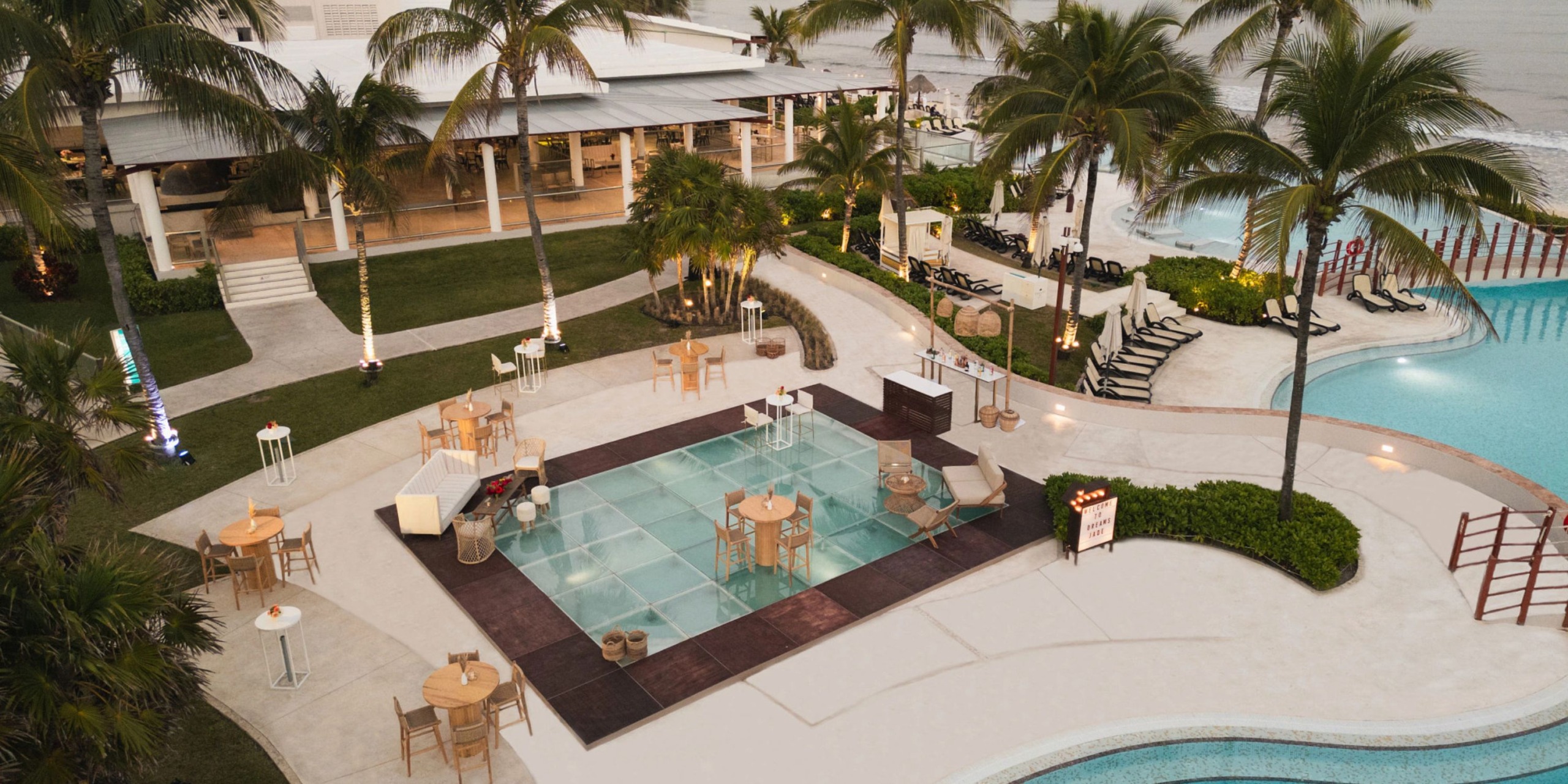 Aerial view of Dreams Jade Riviera Cancun, featuring a glass dance floor, tables set among palm trees, and a pool.
