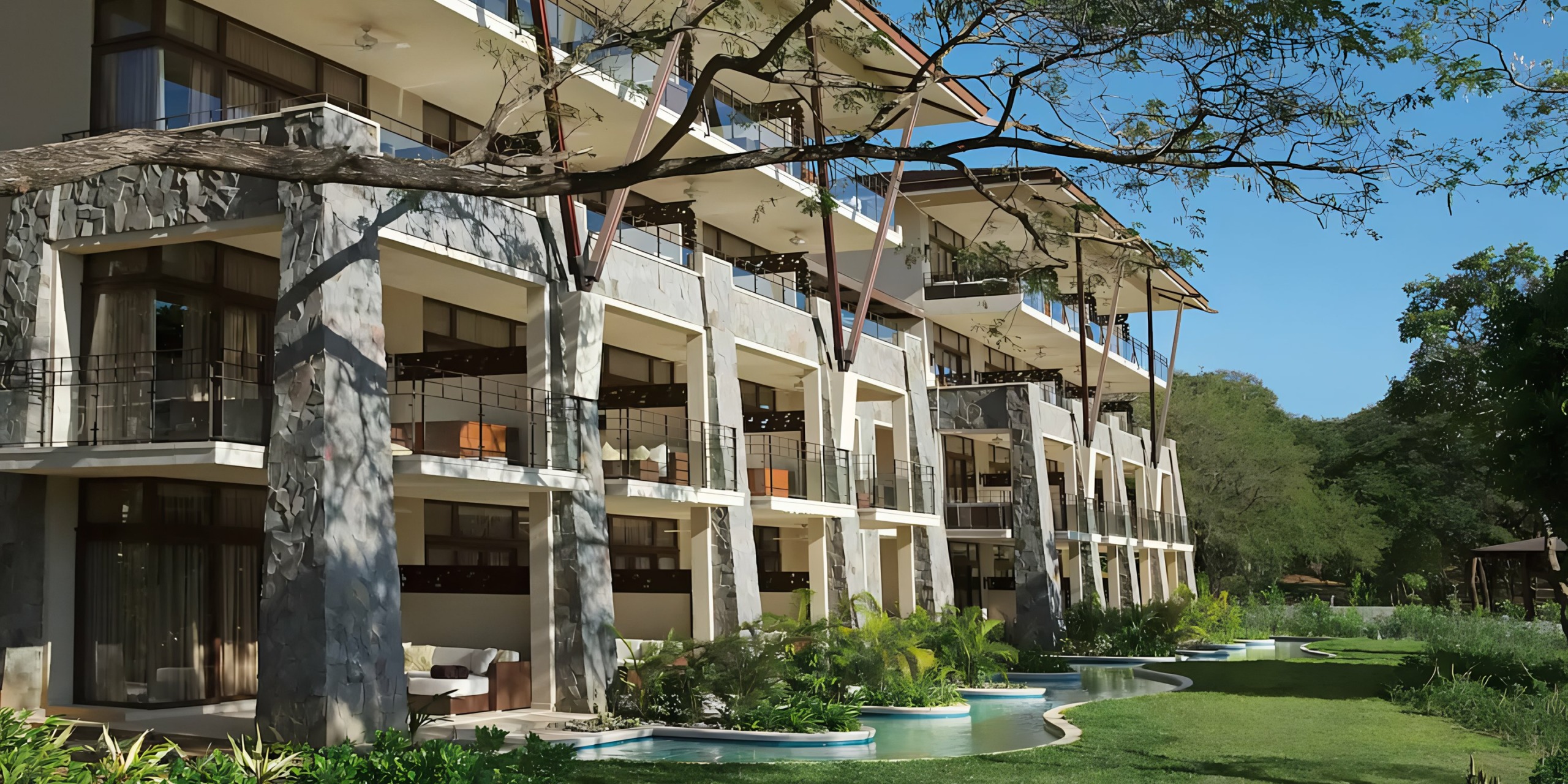 Dreams Las Mareas hotel building with balconies overlooking a meandering pool and lush greenery.