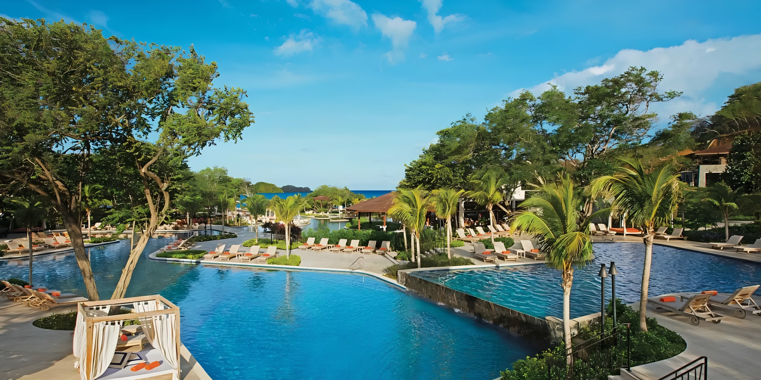 A Dreams Las Mareas swimming pool surrounded by loungers and tropical foliage under a clear blue sky.